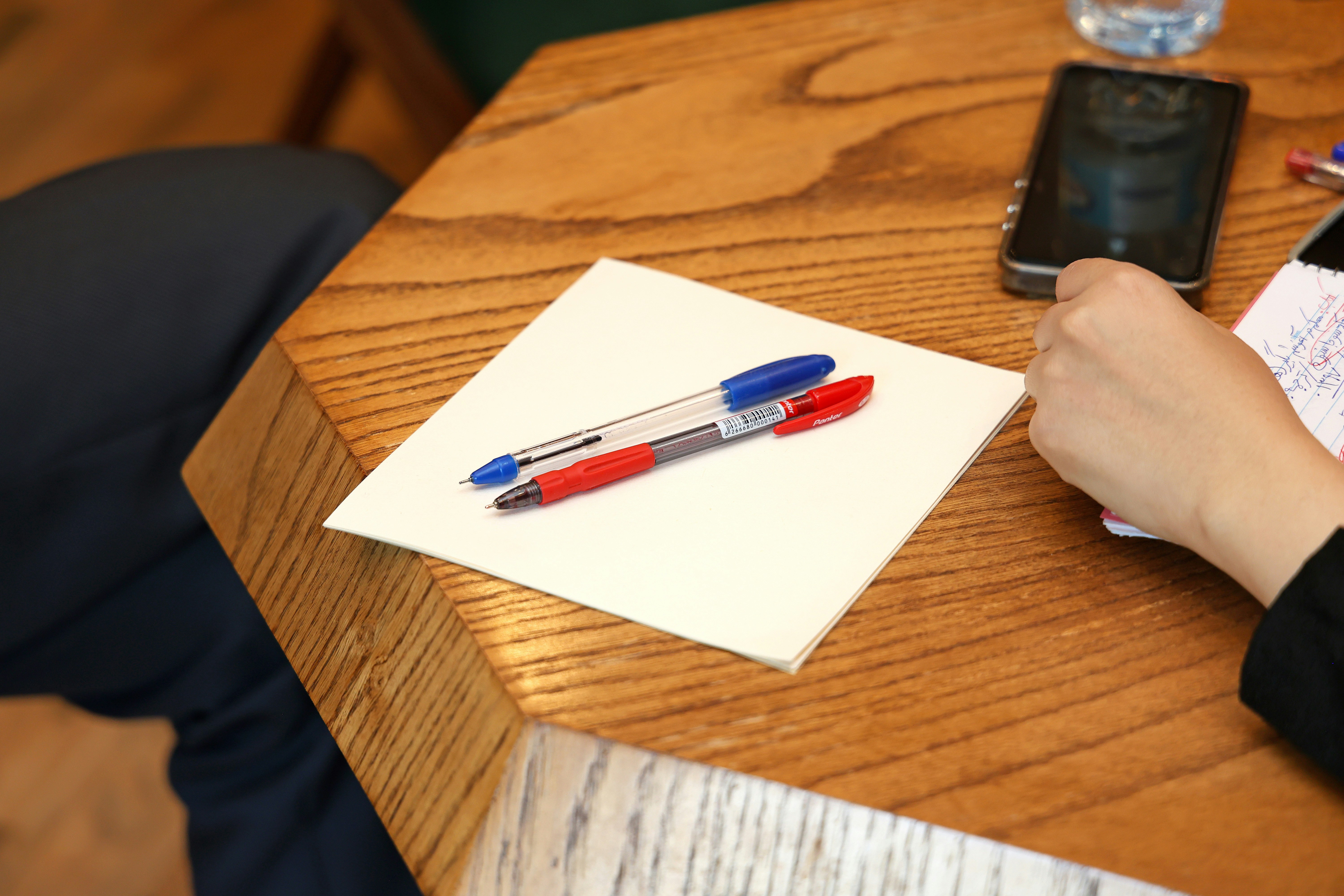 Un bolígrafo rojo y uno azul sobre una libreta blanca sobre una mesa de madera