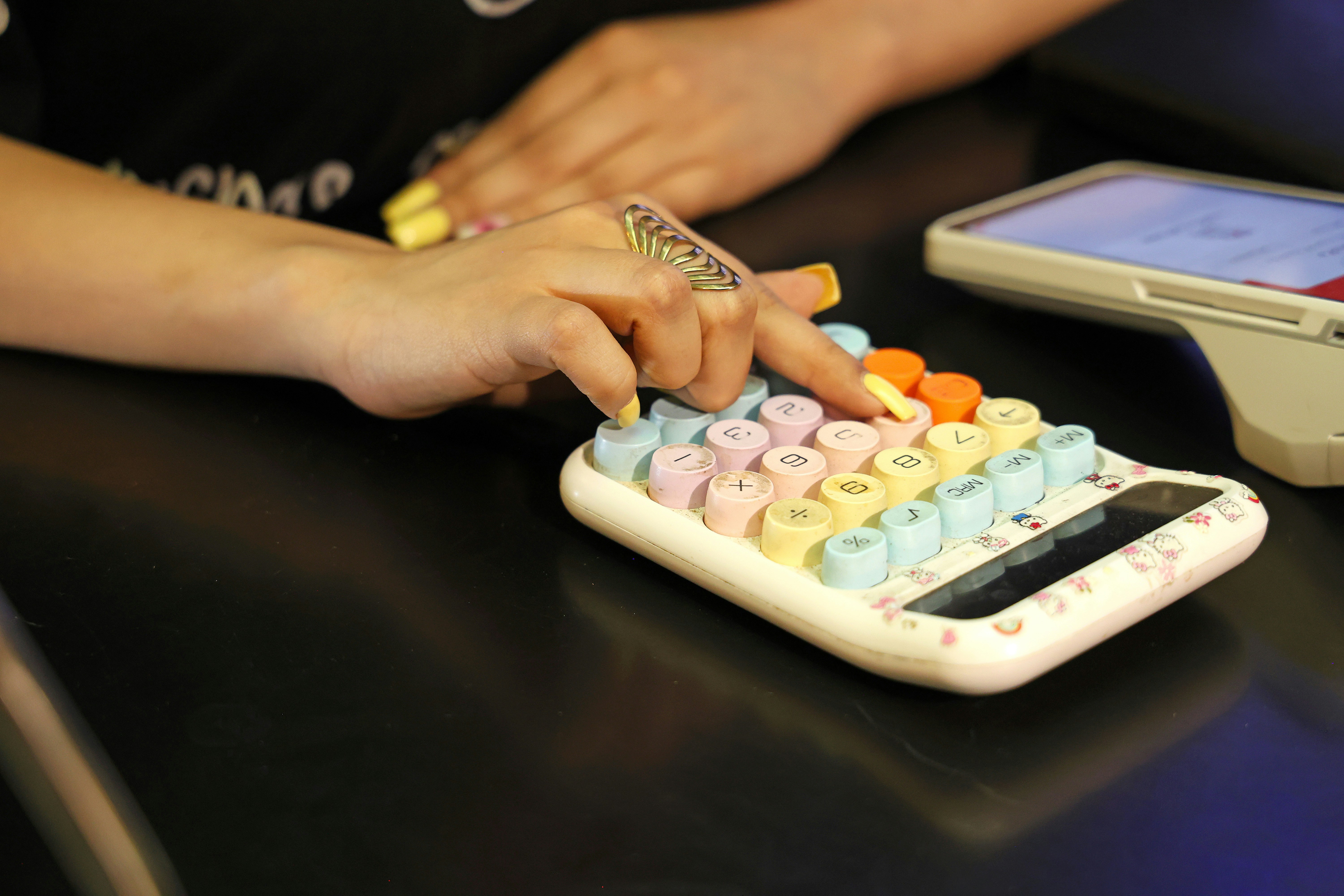 Una persona con uñas amarillas pulsando botones en una calculadora pastel de colores