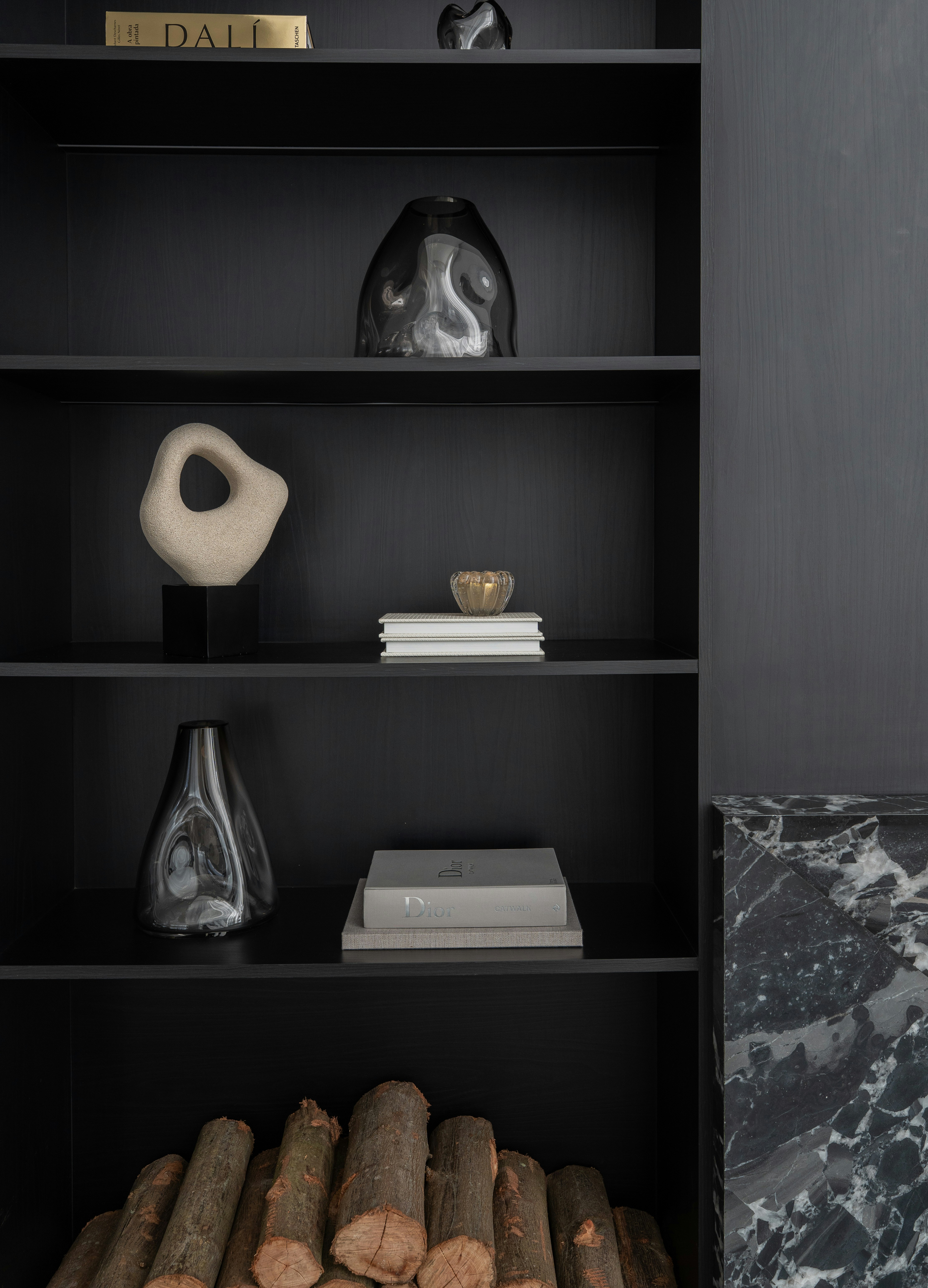 Decorative objects and books on black shelves beside a marble fireplace with firewood