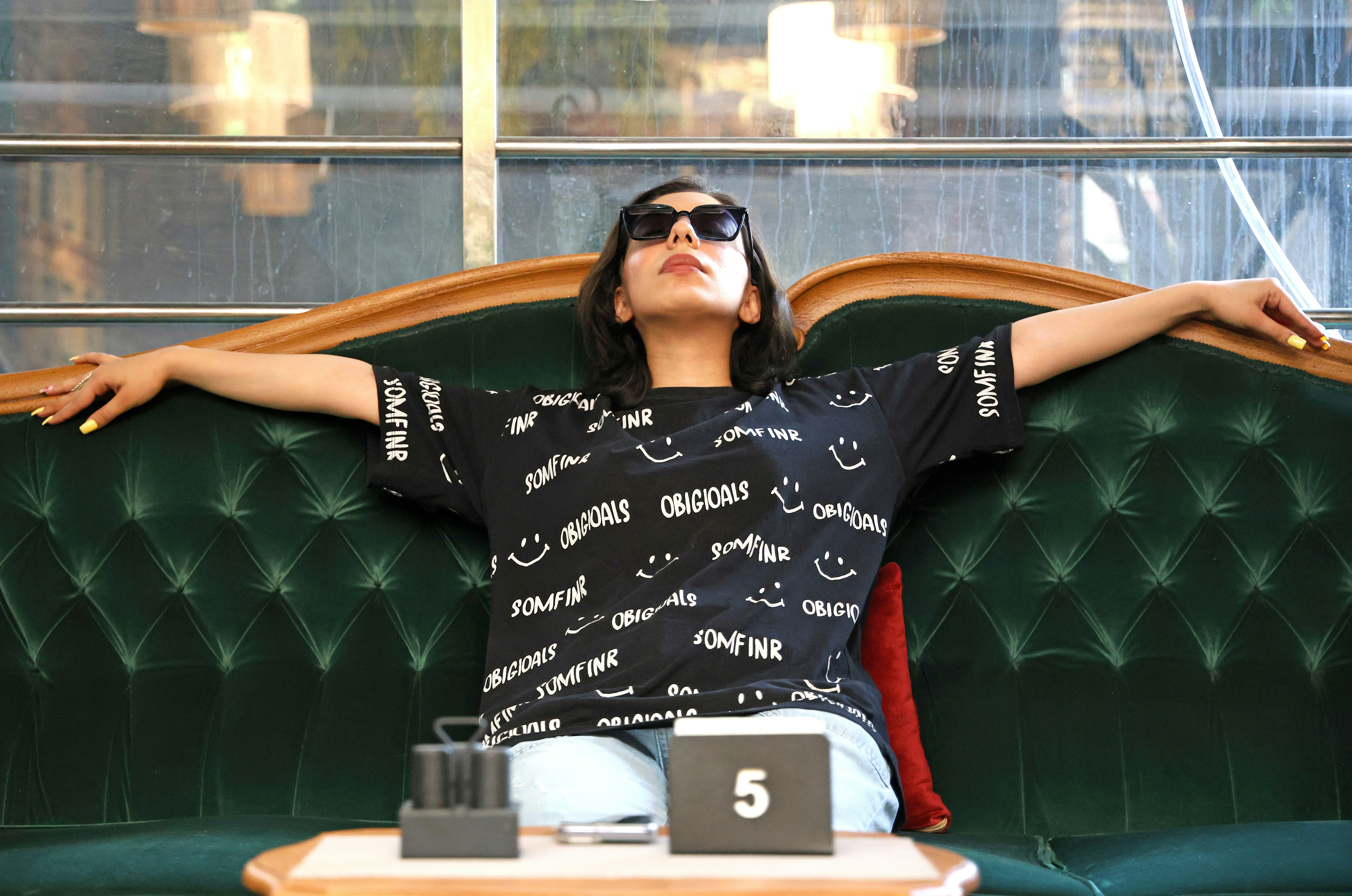 Una mujer con gafas de sol y una camiseta negra con estampado relajándose en un sofá verde