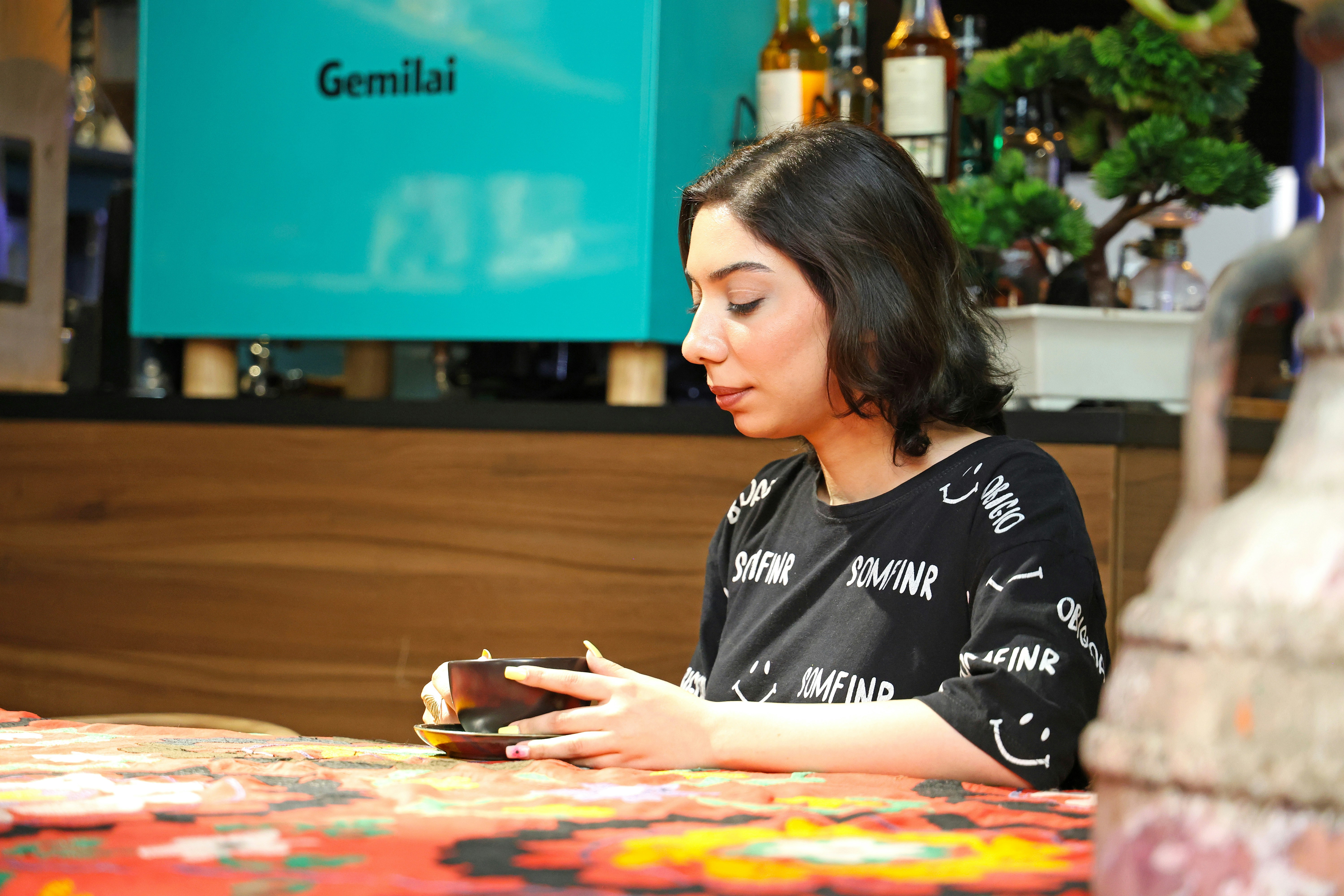 Una mujer con una camisa negra con estampados sosteniendo una taza en una mesa