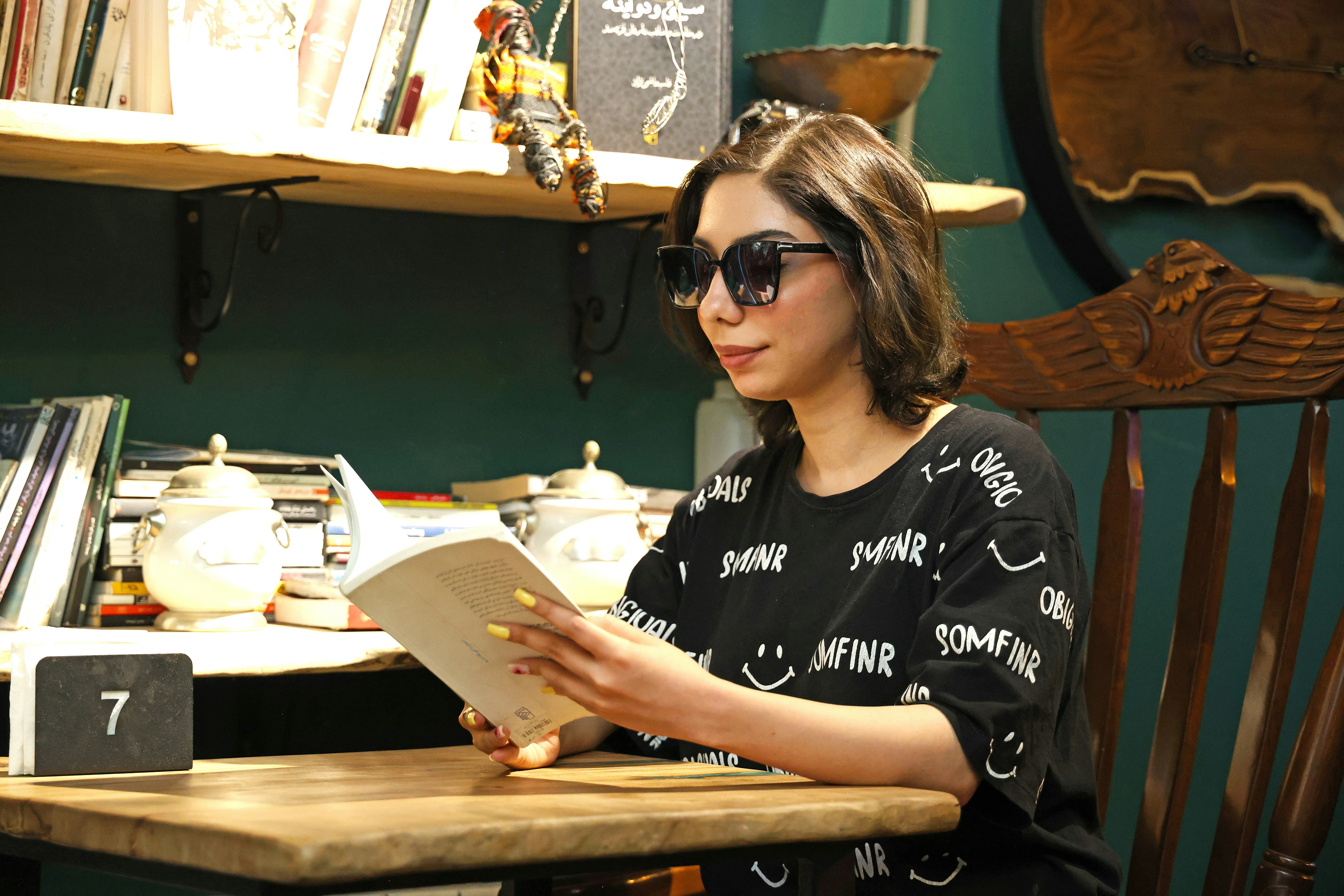 Una mujer con gafas de sol leyendo un libro en una mesa de madera en una biblioteca