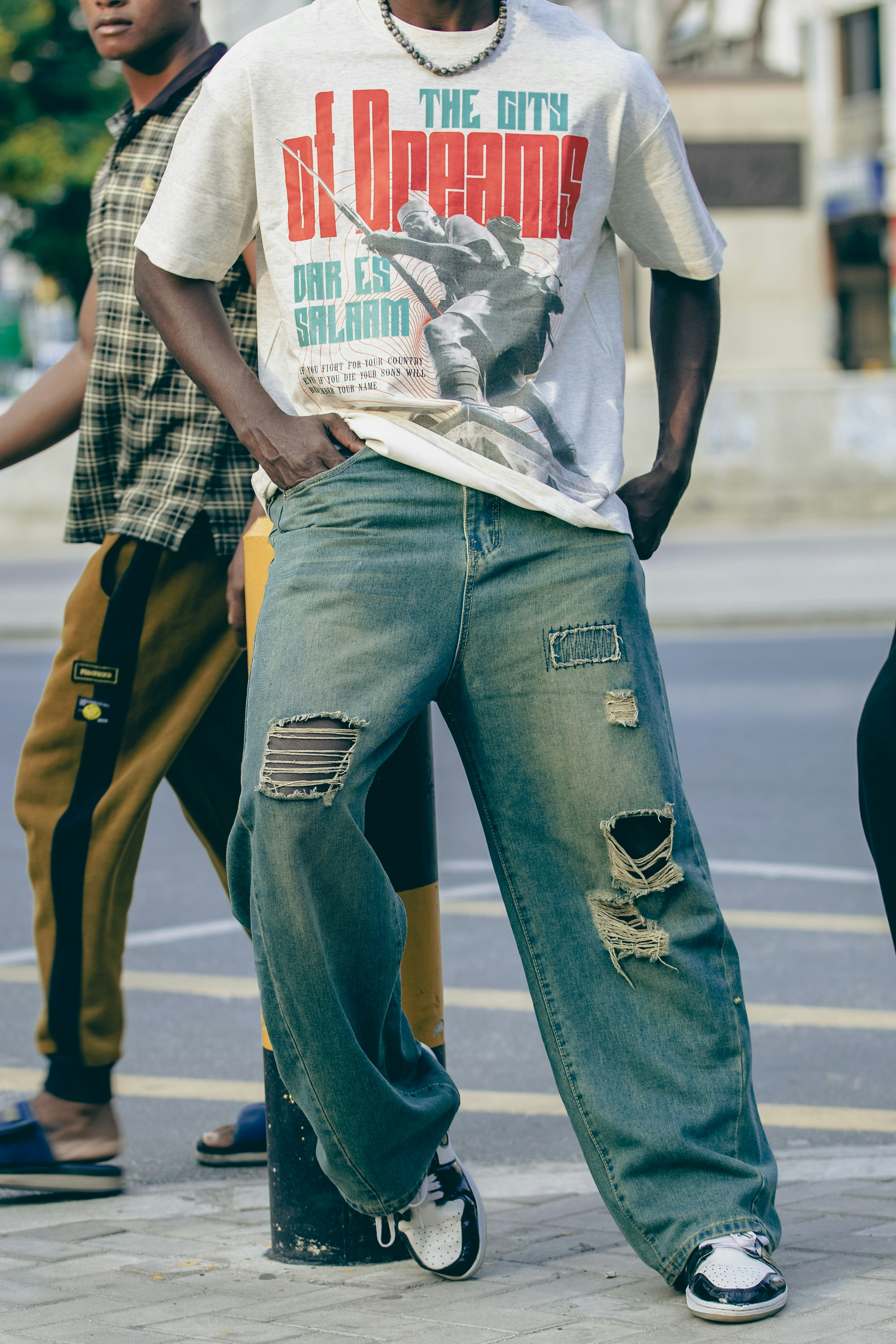 A person wearing a graphic t-shirt and distressed blue jeans on a city street