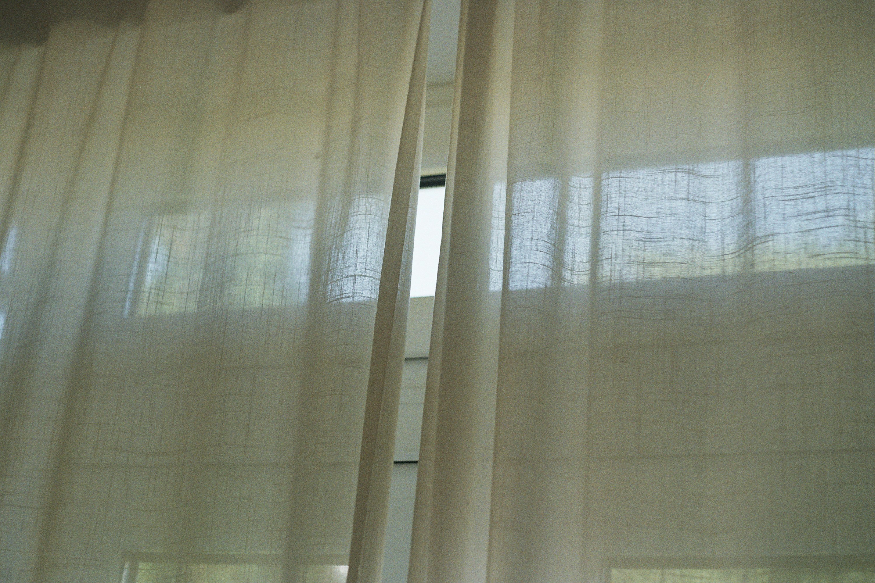 Sheer white linen curtains hanging in front of a bright window, daylight showing through the weave