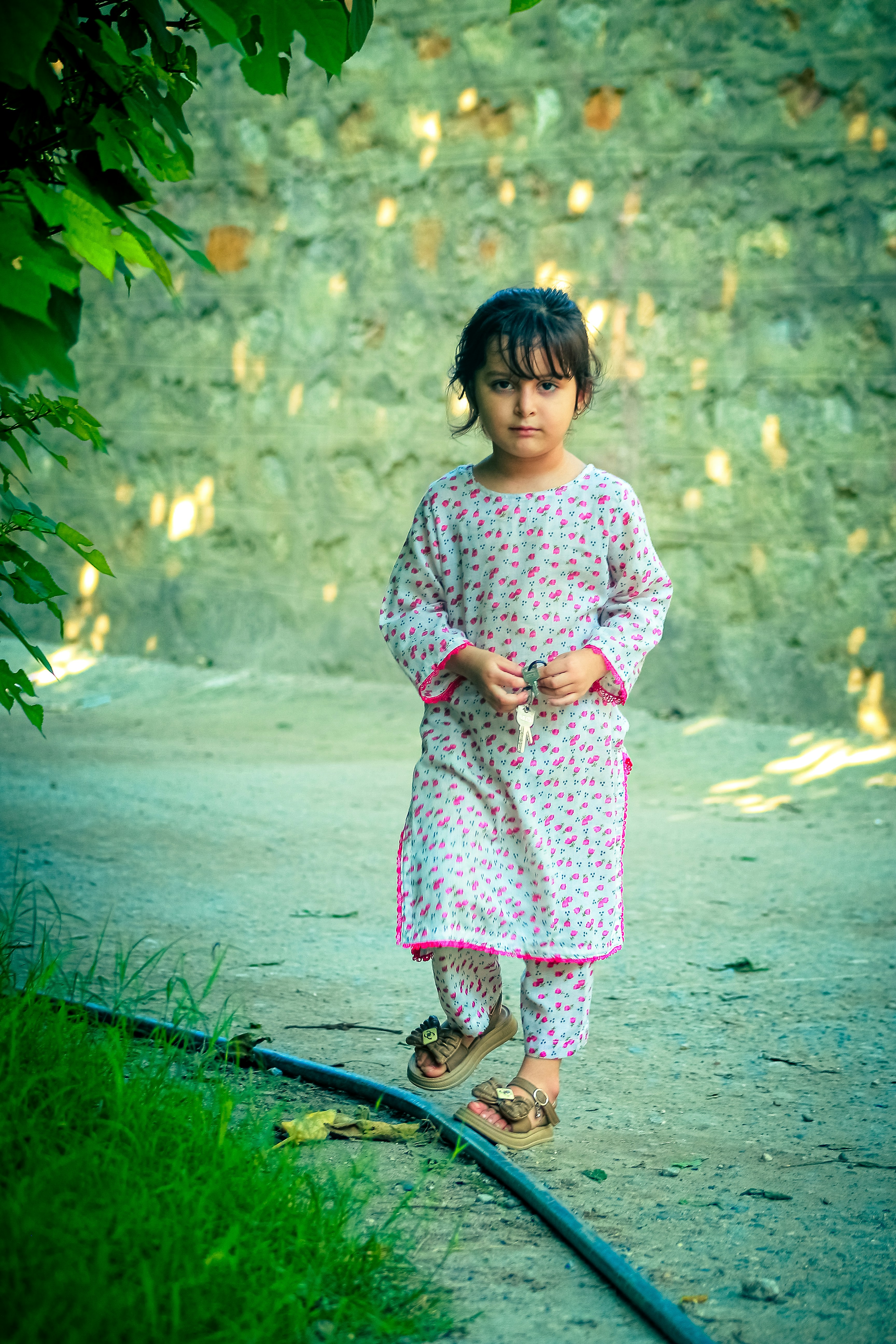 A child in a patterned tunic and trousers holding keys on a path