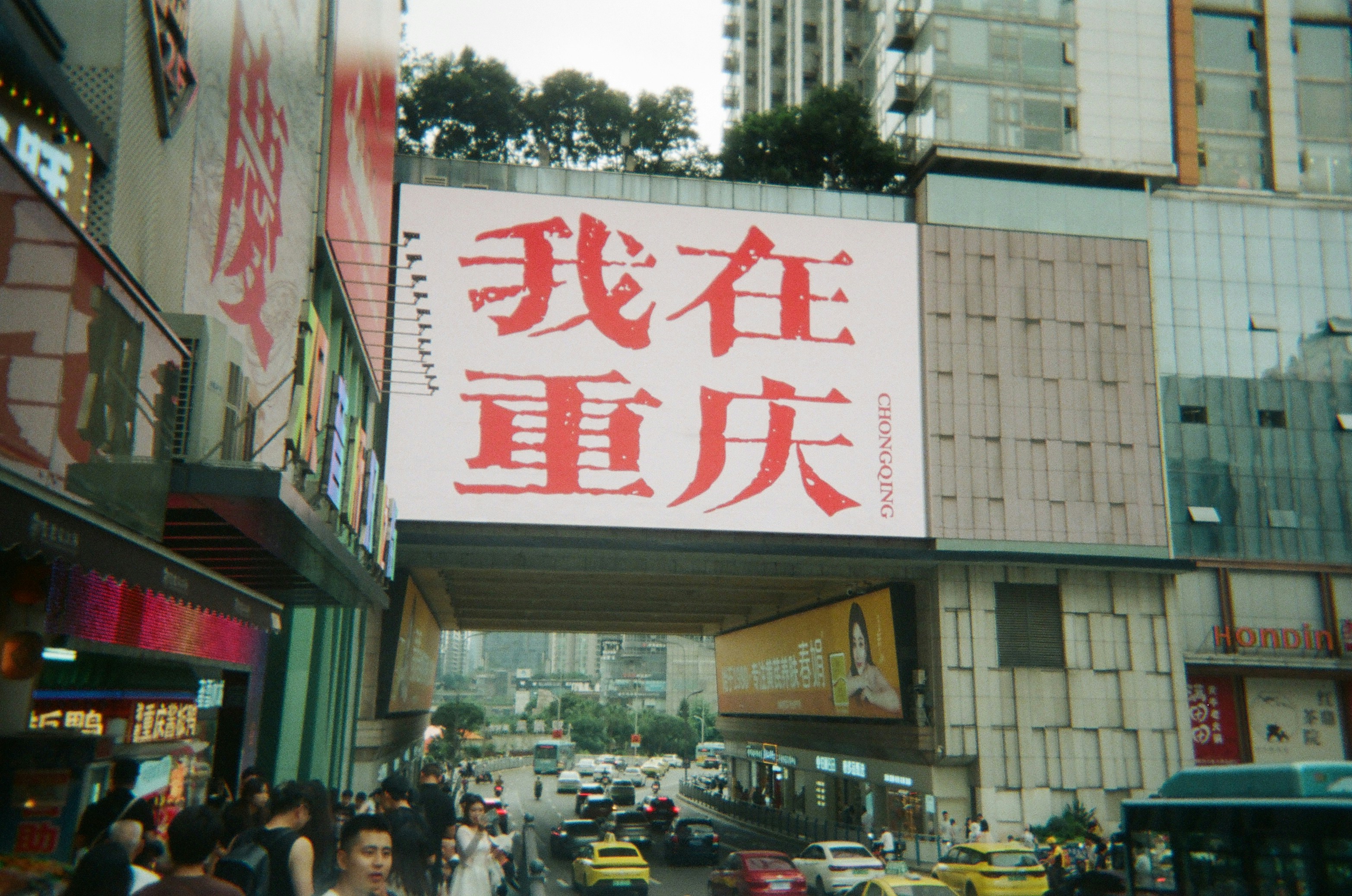 A large billboard with red Chinese characters above a busy street in Chongqing