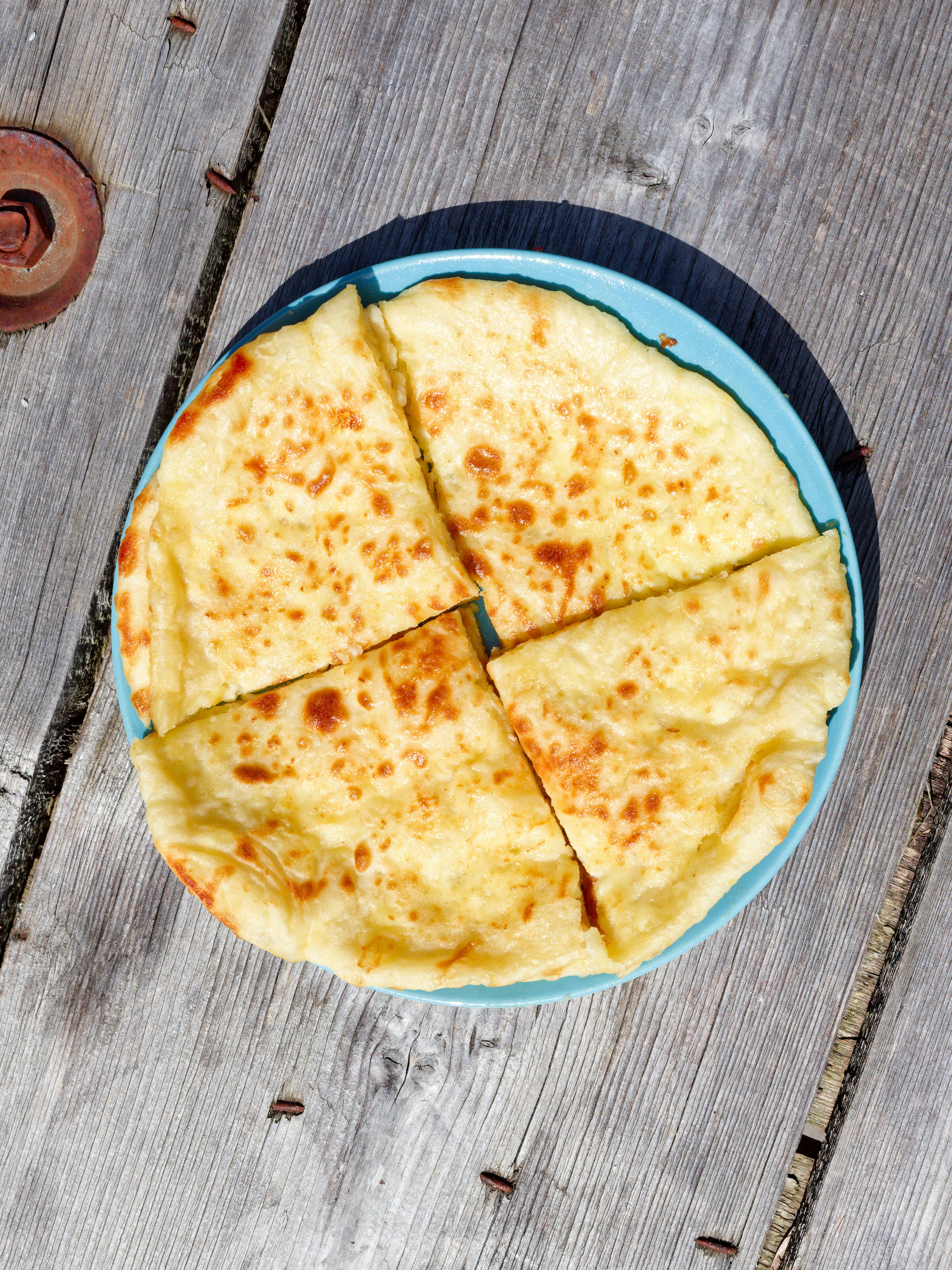 A sliced cheese flatbread on a blue plate atop a weathered wooden surface