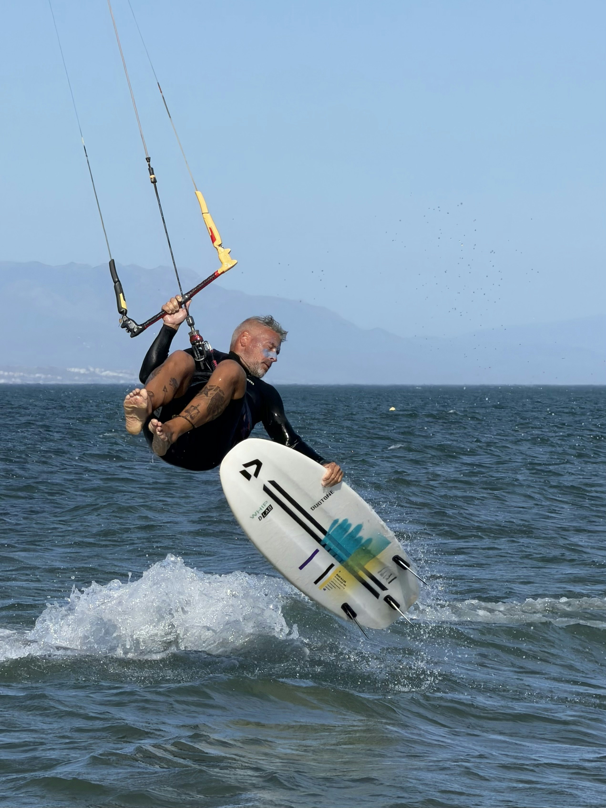 A person kitesurfing, jumping high above the ocean waves with a board