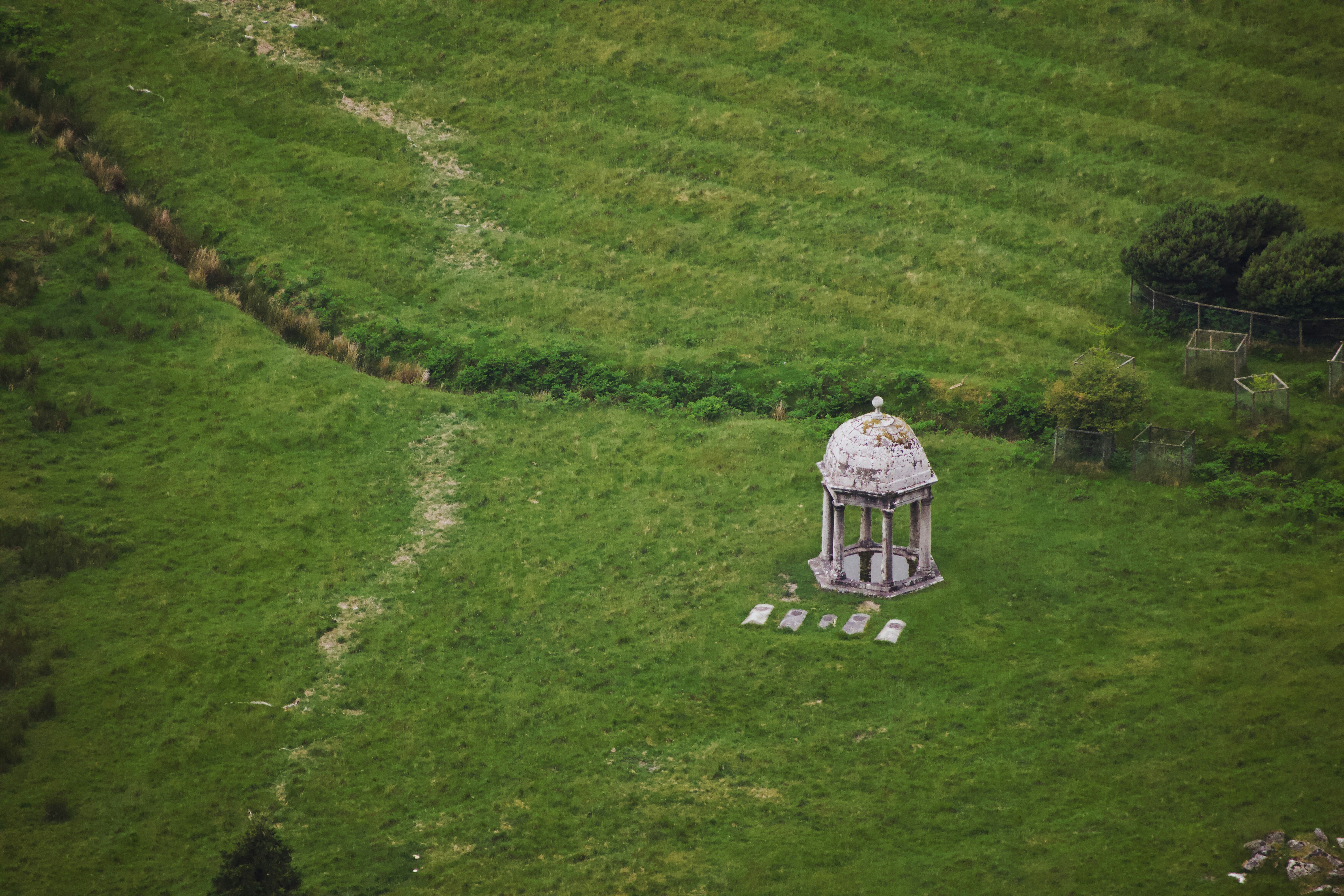 A stone gazebo and four grave markers in a vast green field