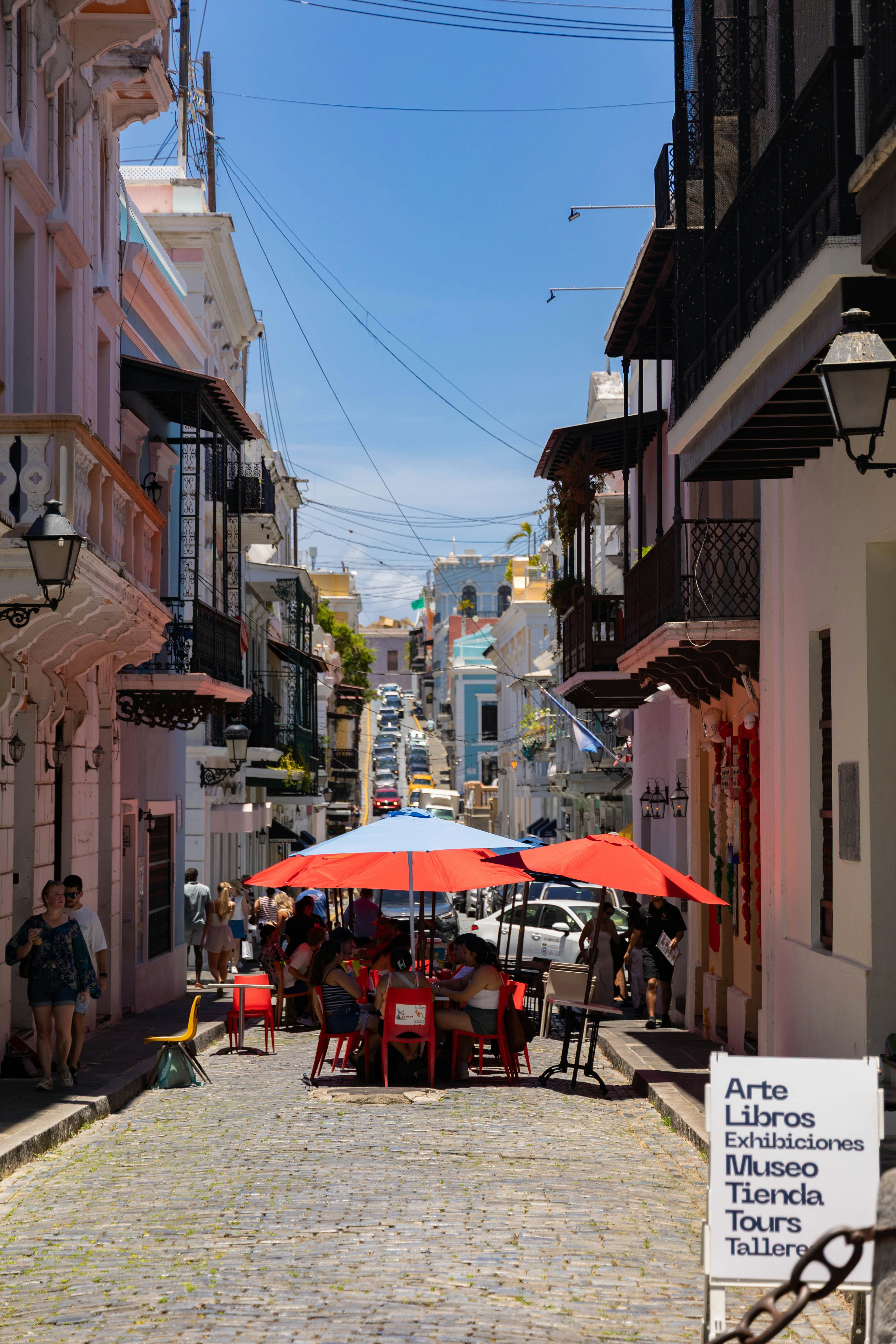 People dining under red umbrellas on a cobblestone street in Old San Juan