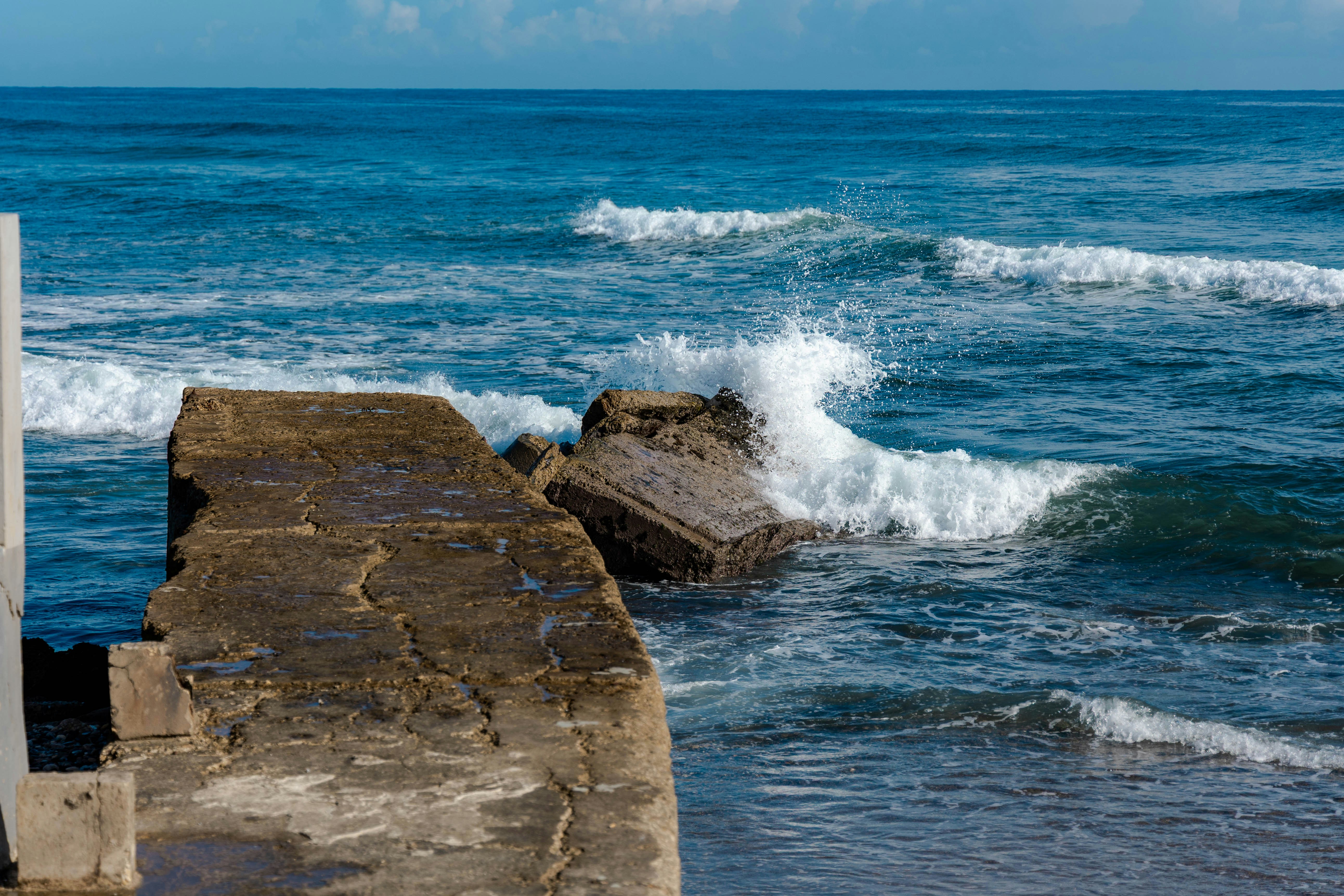 Waves crashing against a weathered concrete pier in the blue ocean