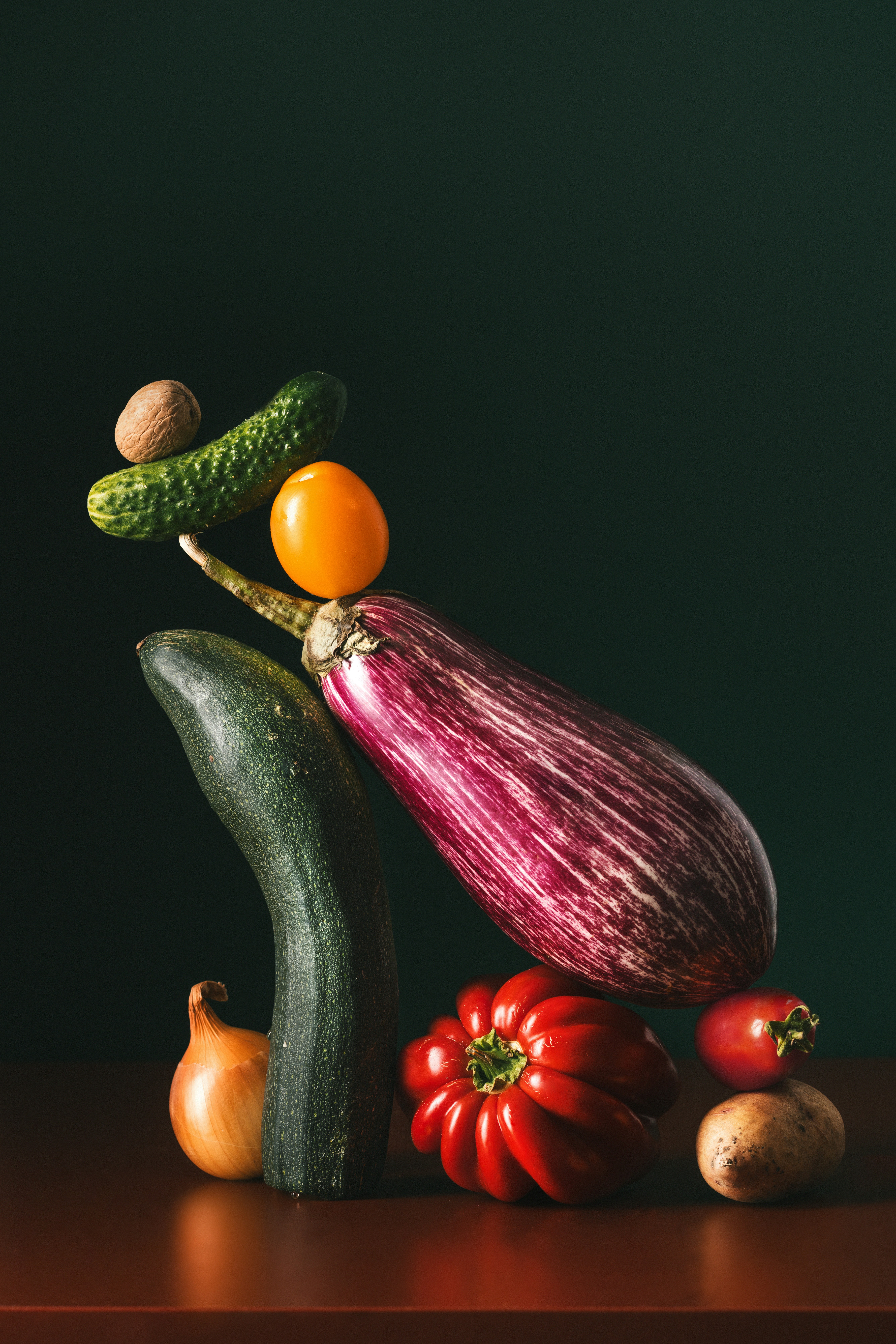 A balanced stack of eggplant, zucchini, tomato, cucumber, onion, potato, and walnut