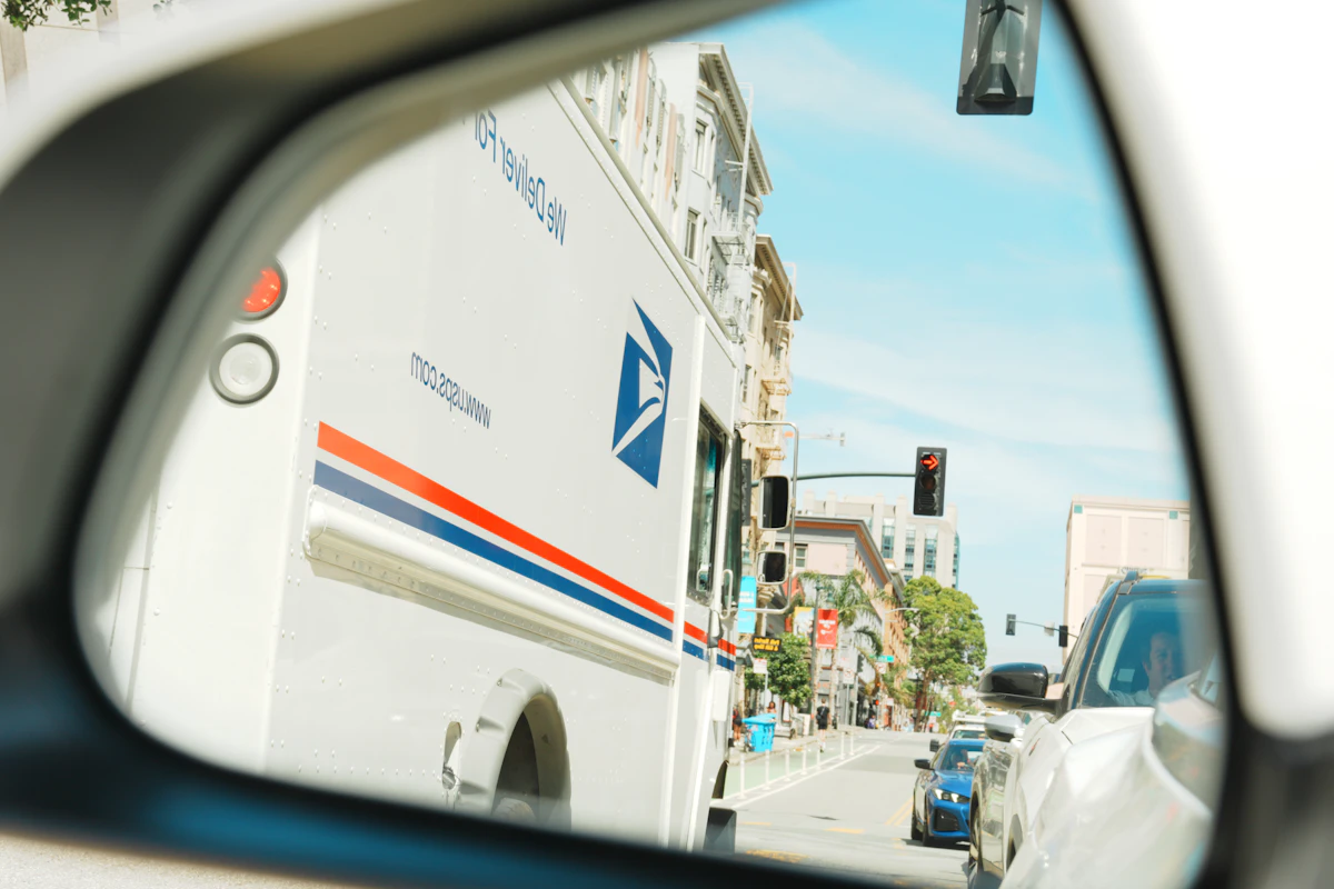 A mail truck reflected in a car side mirror on a city street