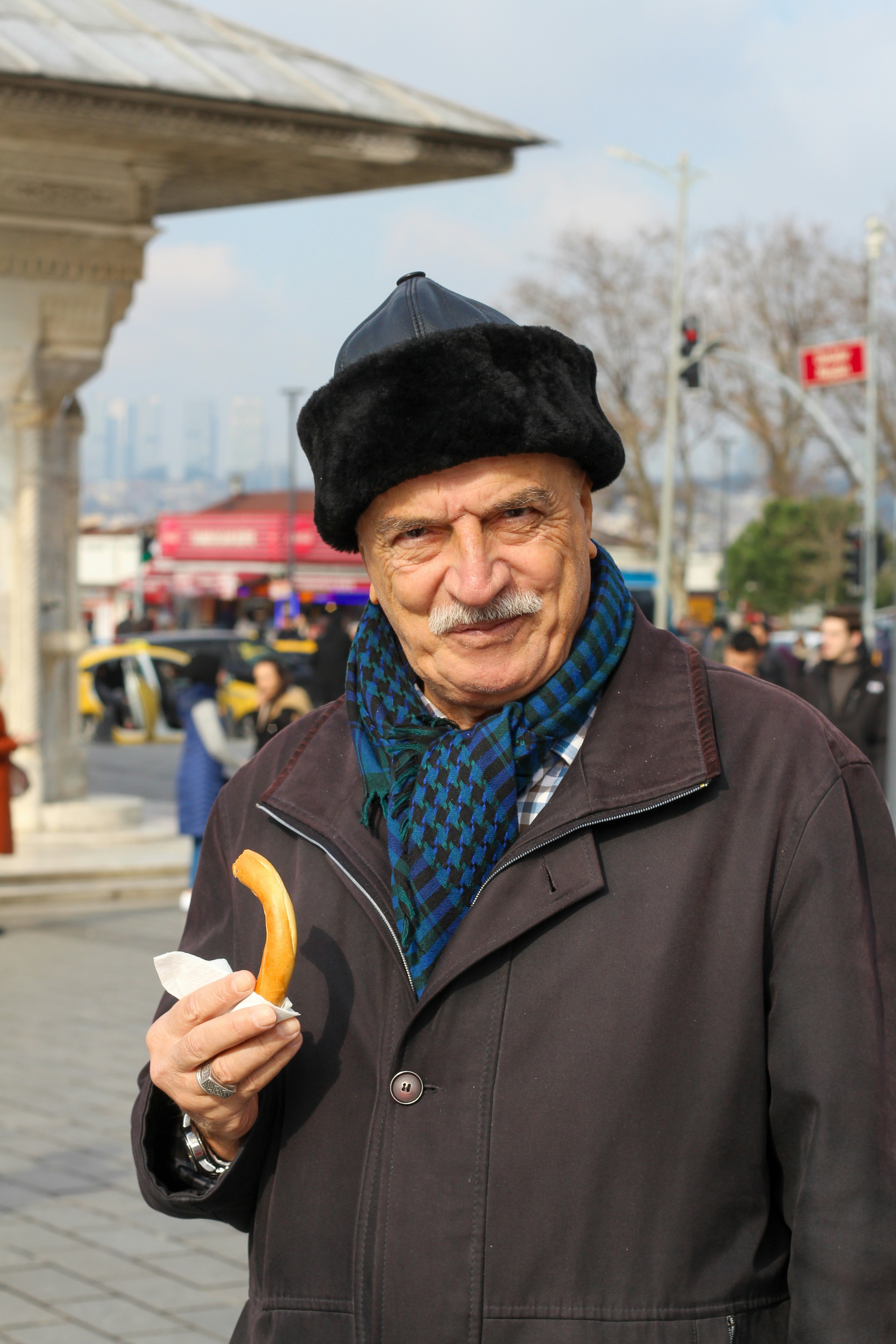 older man in fur hat and scarf holding a pastry on Istanbul street