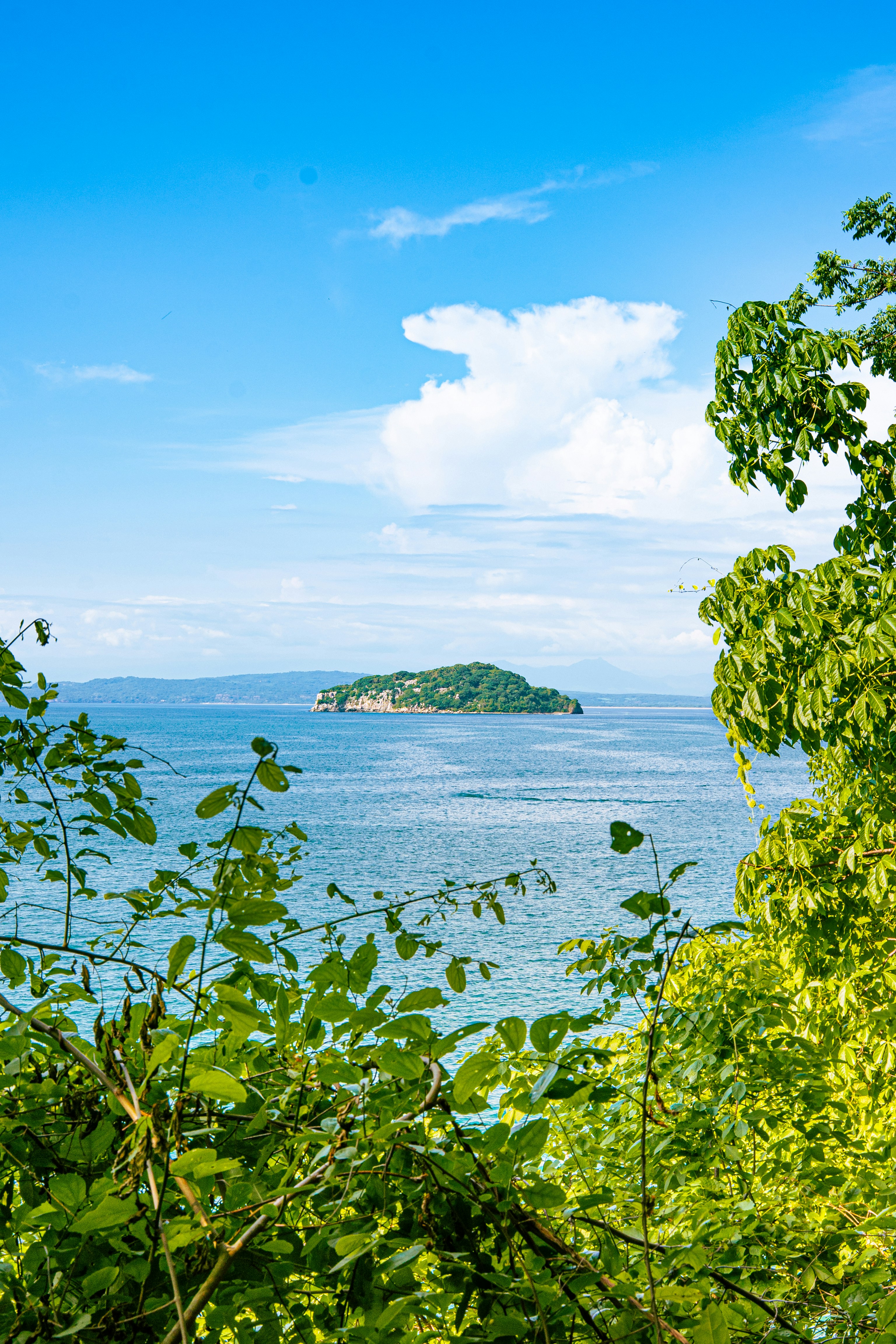 A small green island in the middle of a blue ocean under a bright sky