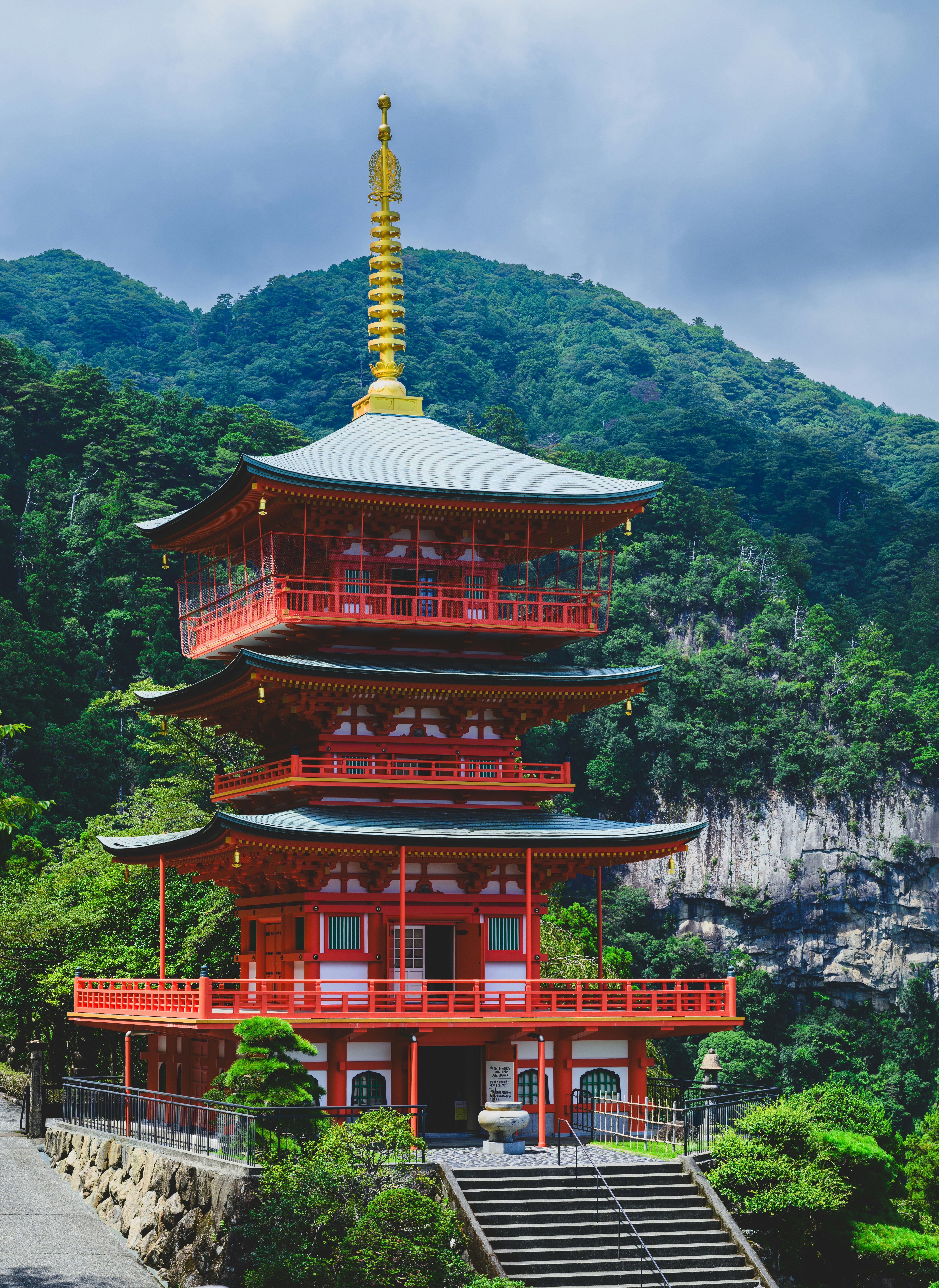 Um pagode vermelho de três andares com uma torre dourada contra uma montanha verde exuberante