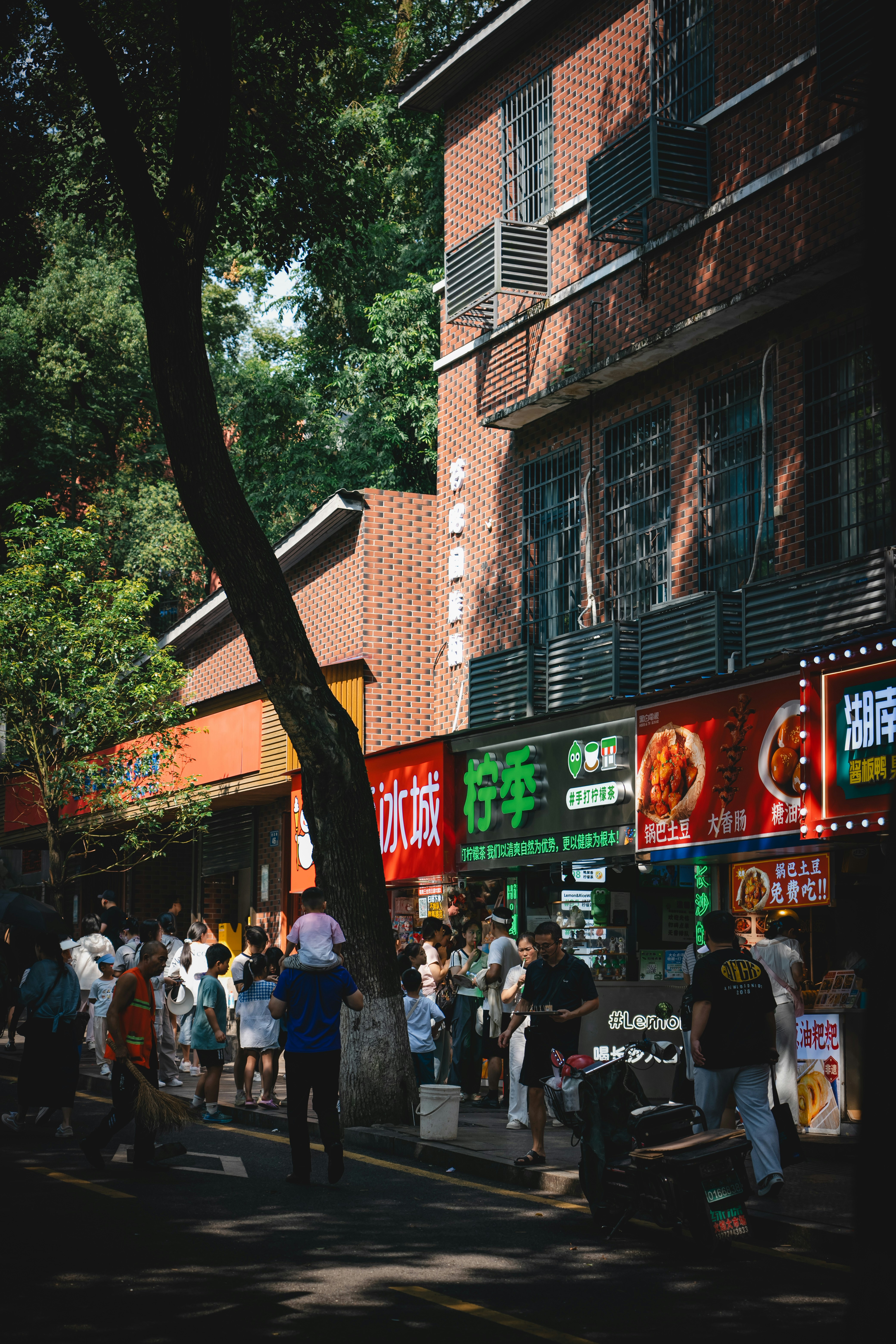 People walking along a busy street lined with food stalls and brick buildings