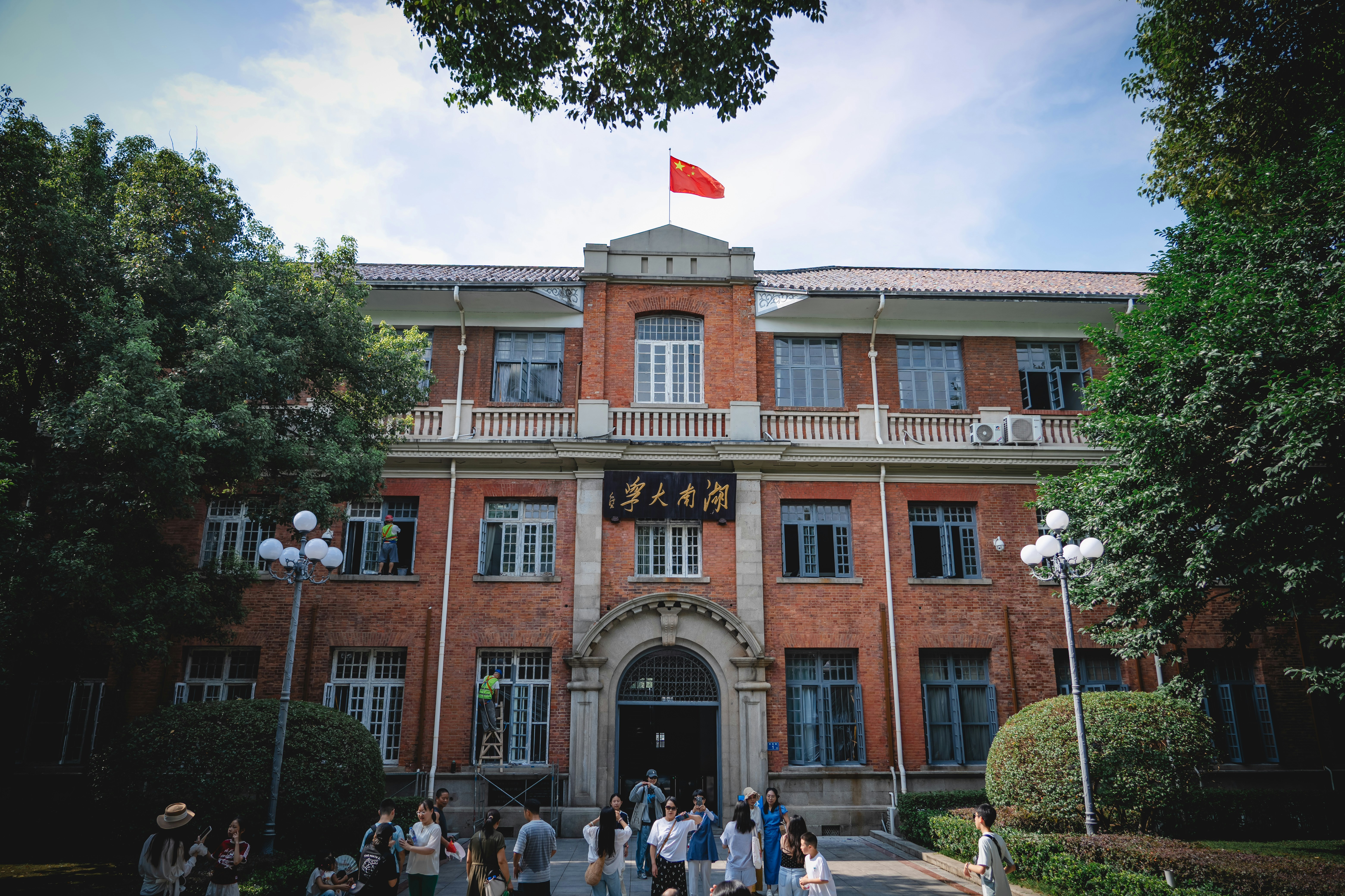 A red brick building with a Chinese flag on the roof and people below