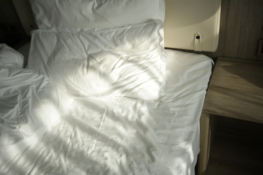 A freshly slept-in hotel bed in morning sunlight