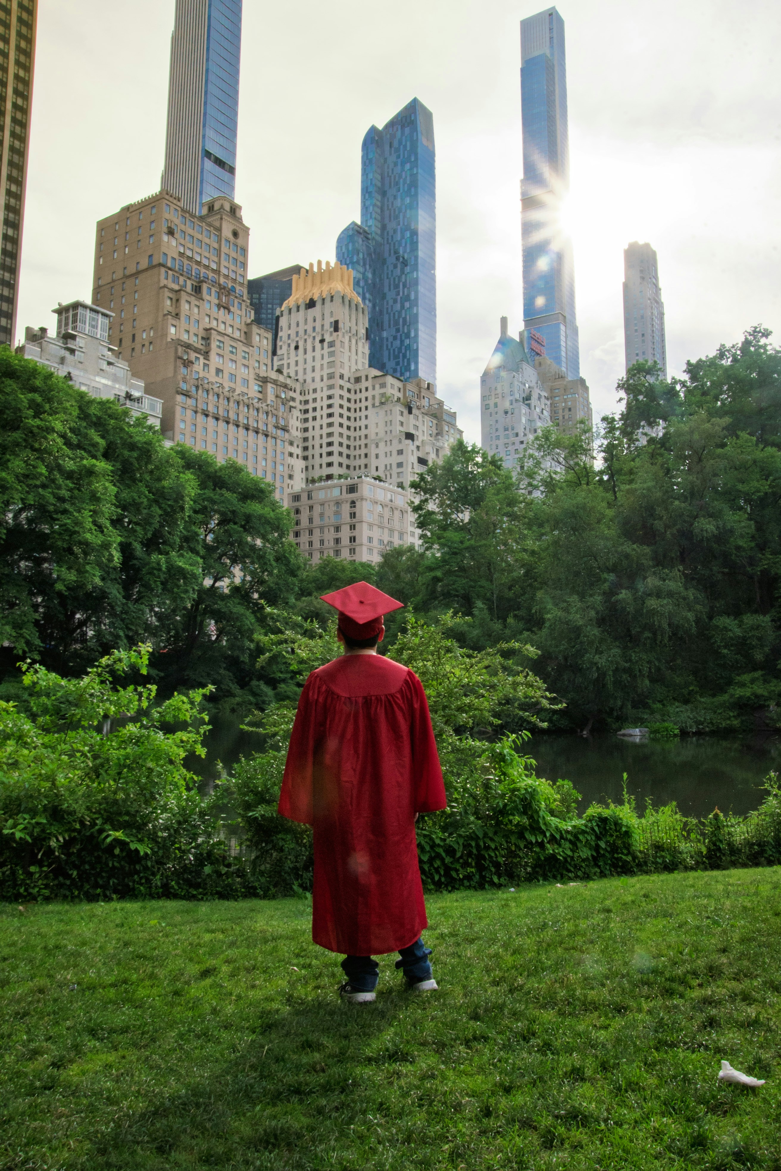 A person in a red graduation gown and cap facing a city skyline