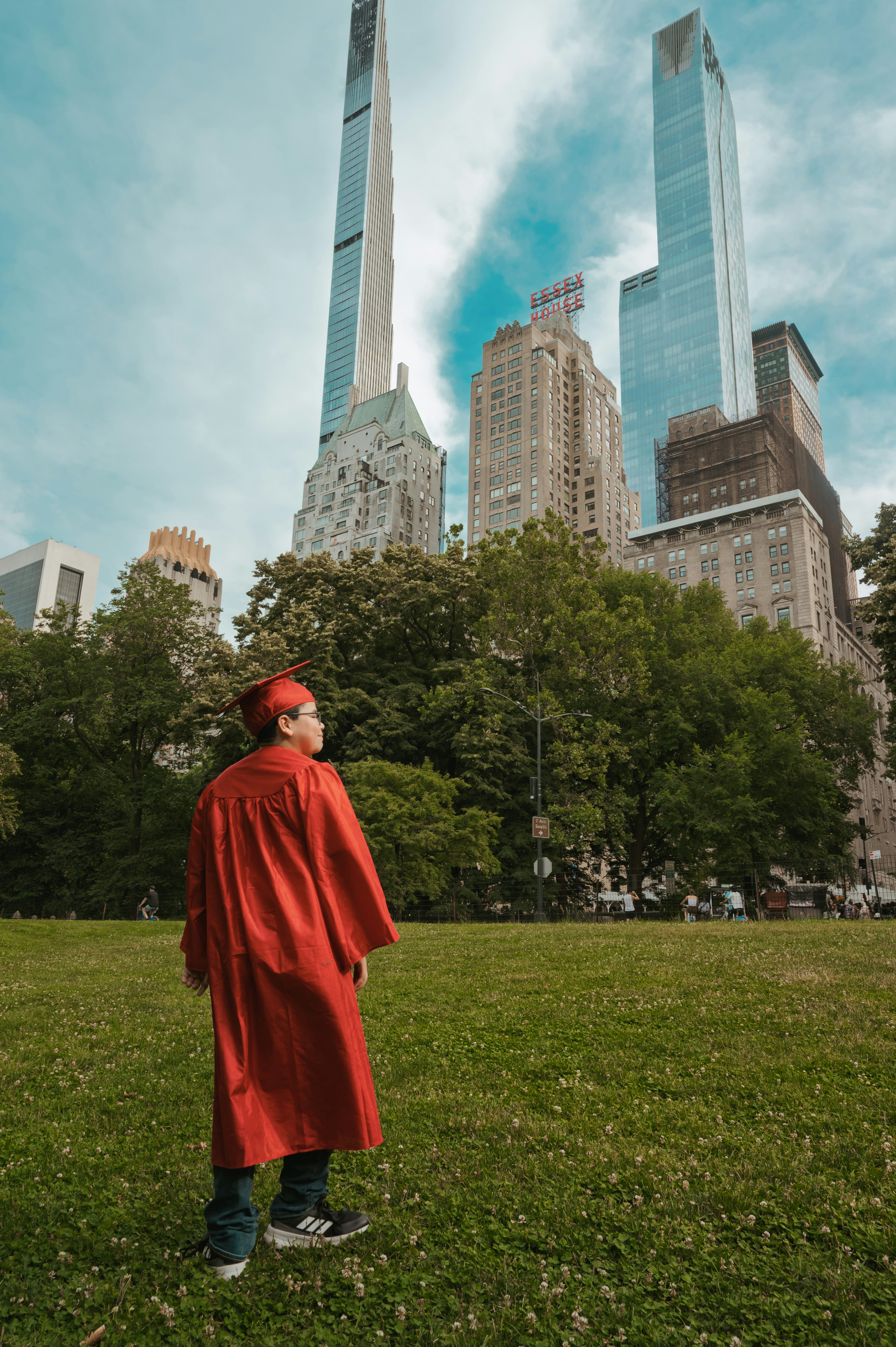 A person in a red graduation gown and cap standing in Central Park, New York