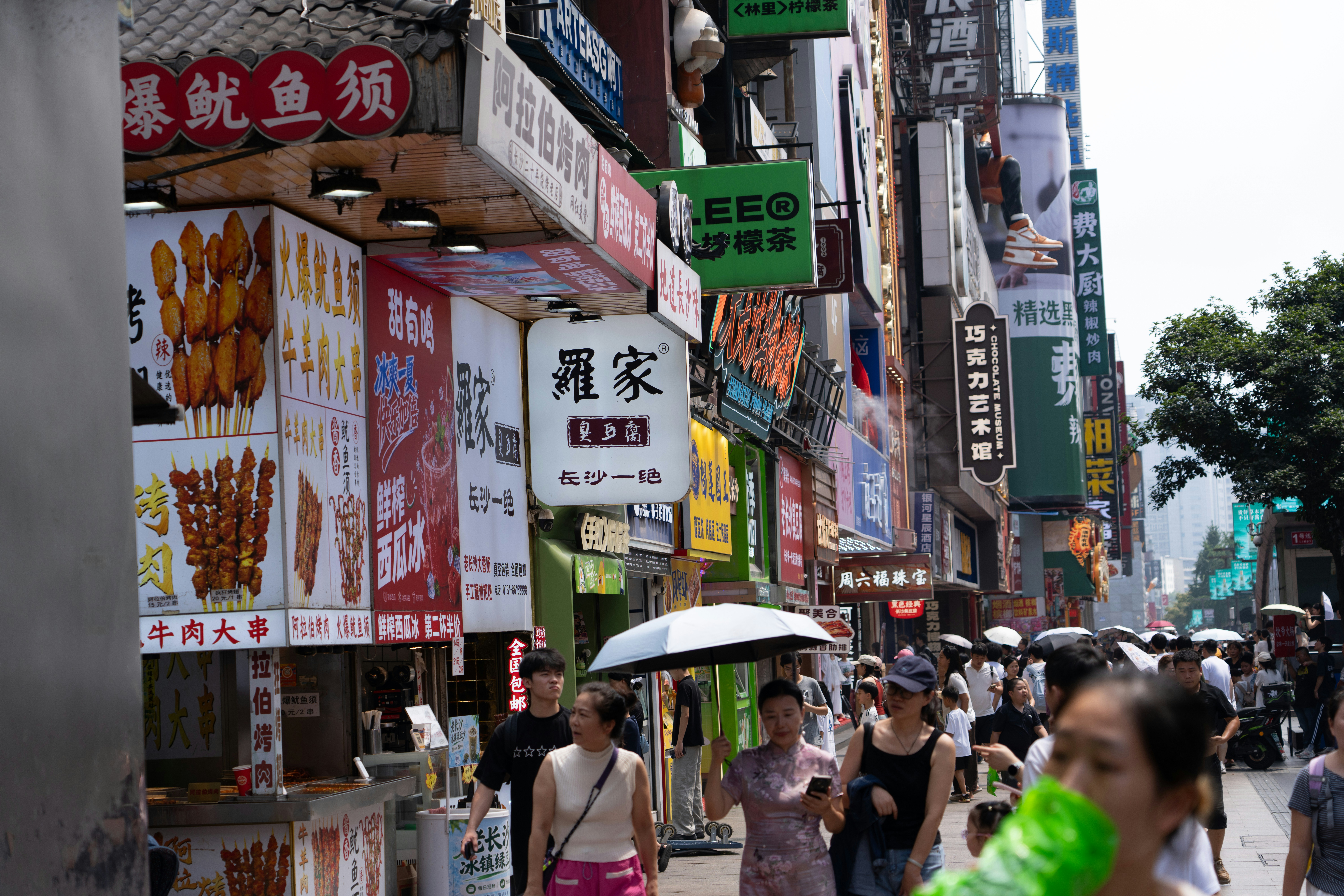 People walking along a busy street lined with colorful food stalls and signs