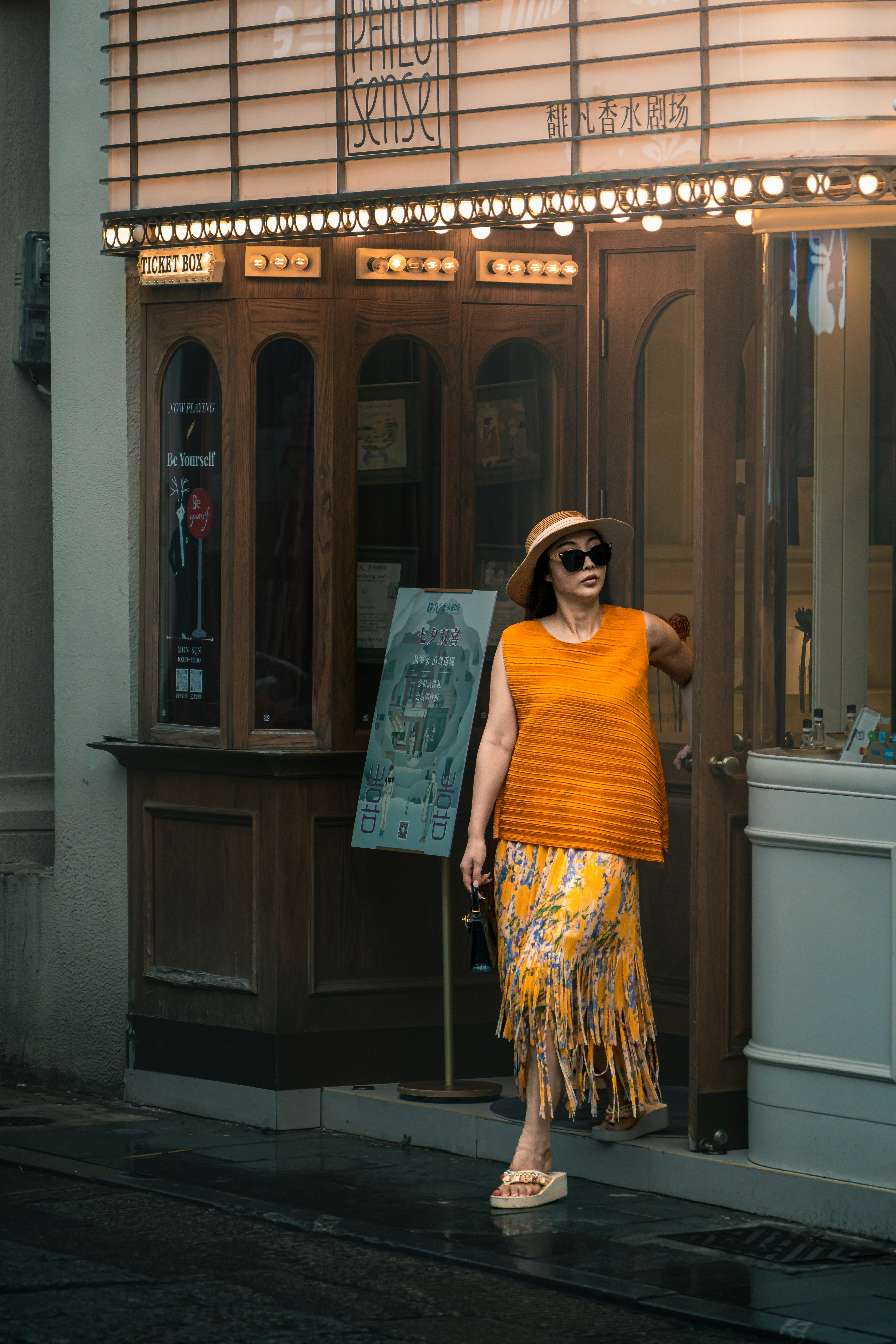 A woman in a straw hat and orange top exiting a theater doorway