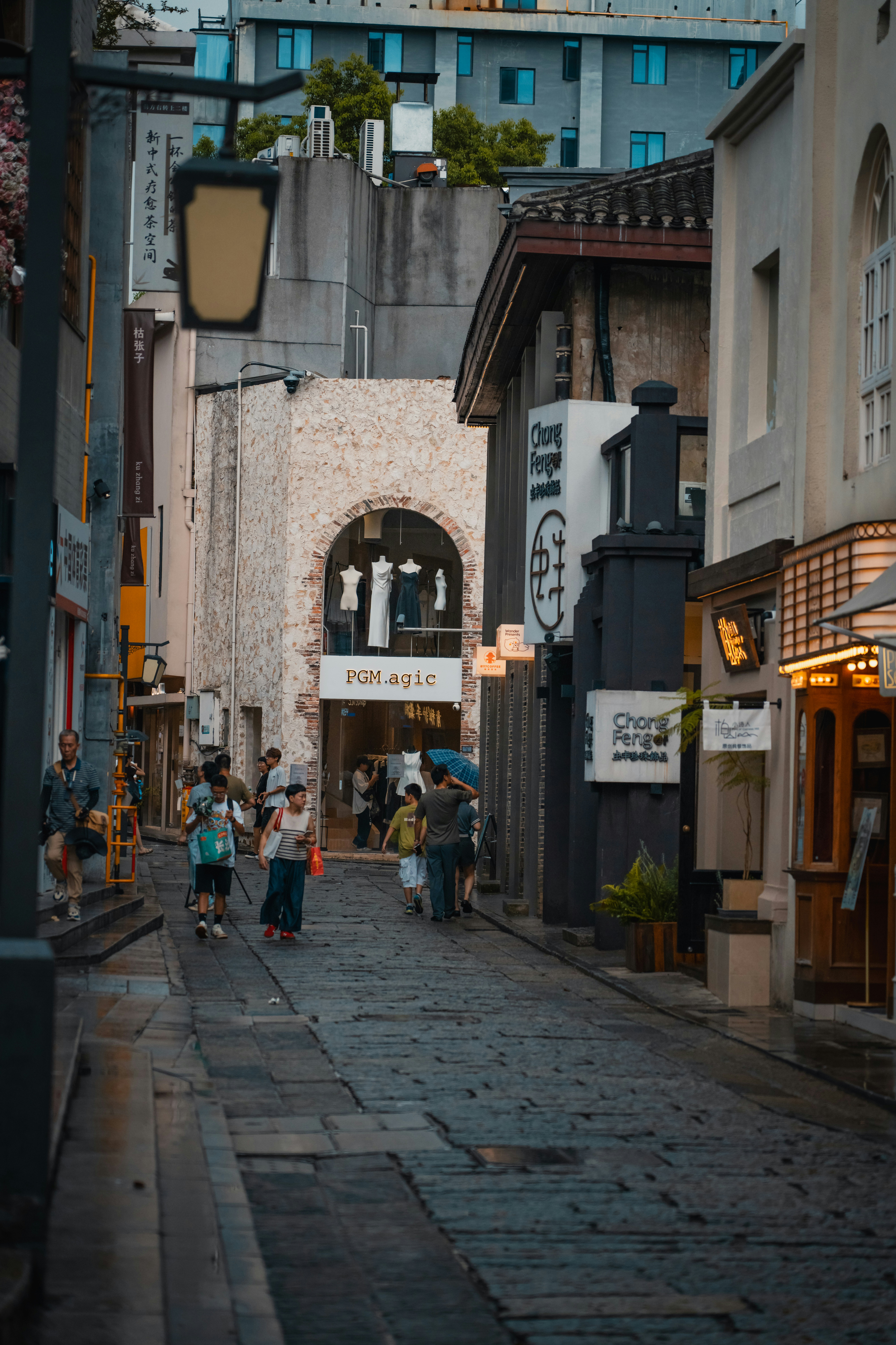 People walking along a narrow stone-paved street lined with shops and signage