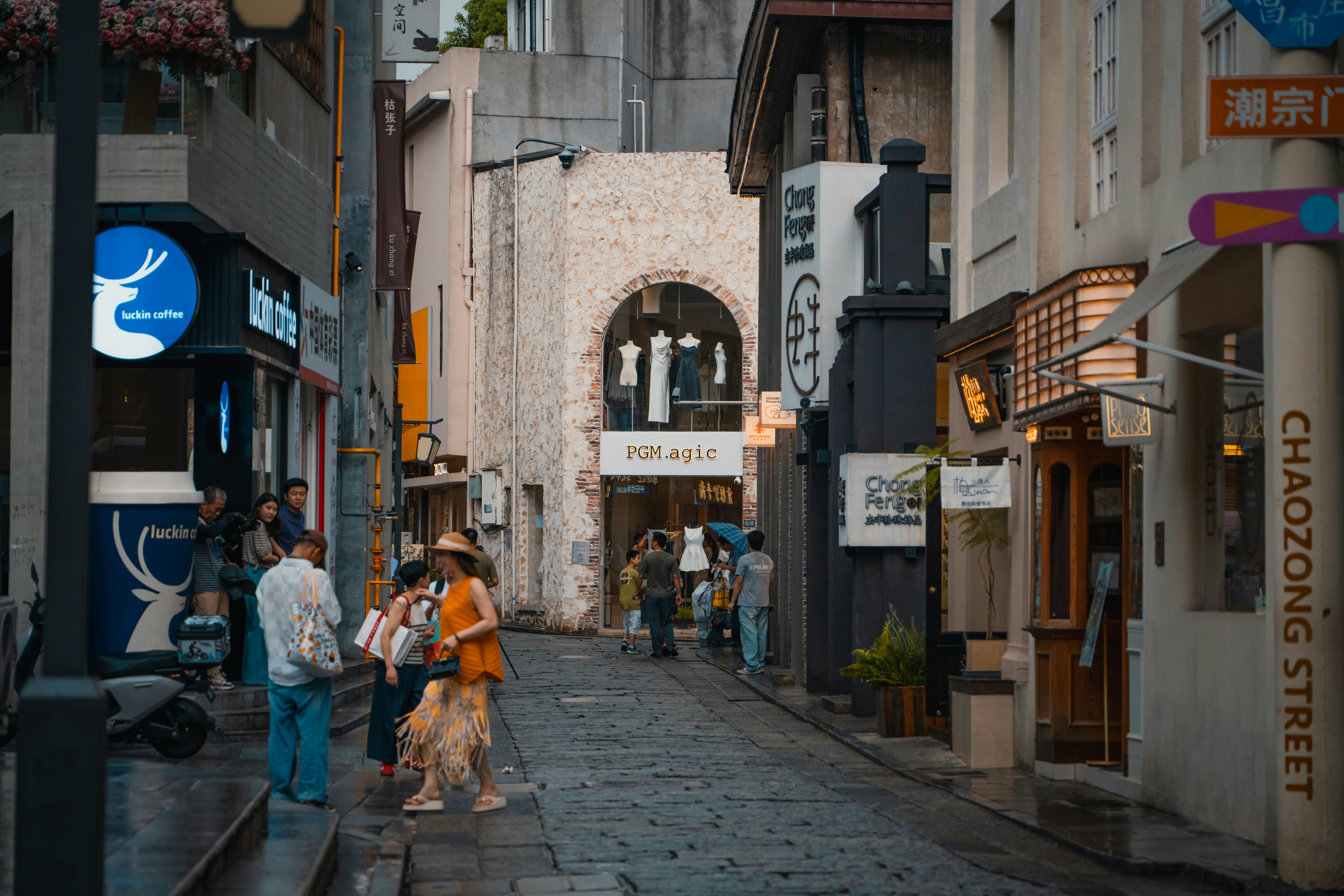 People walking along a narrow stone street lined with shops and cafes