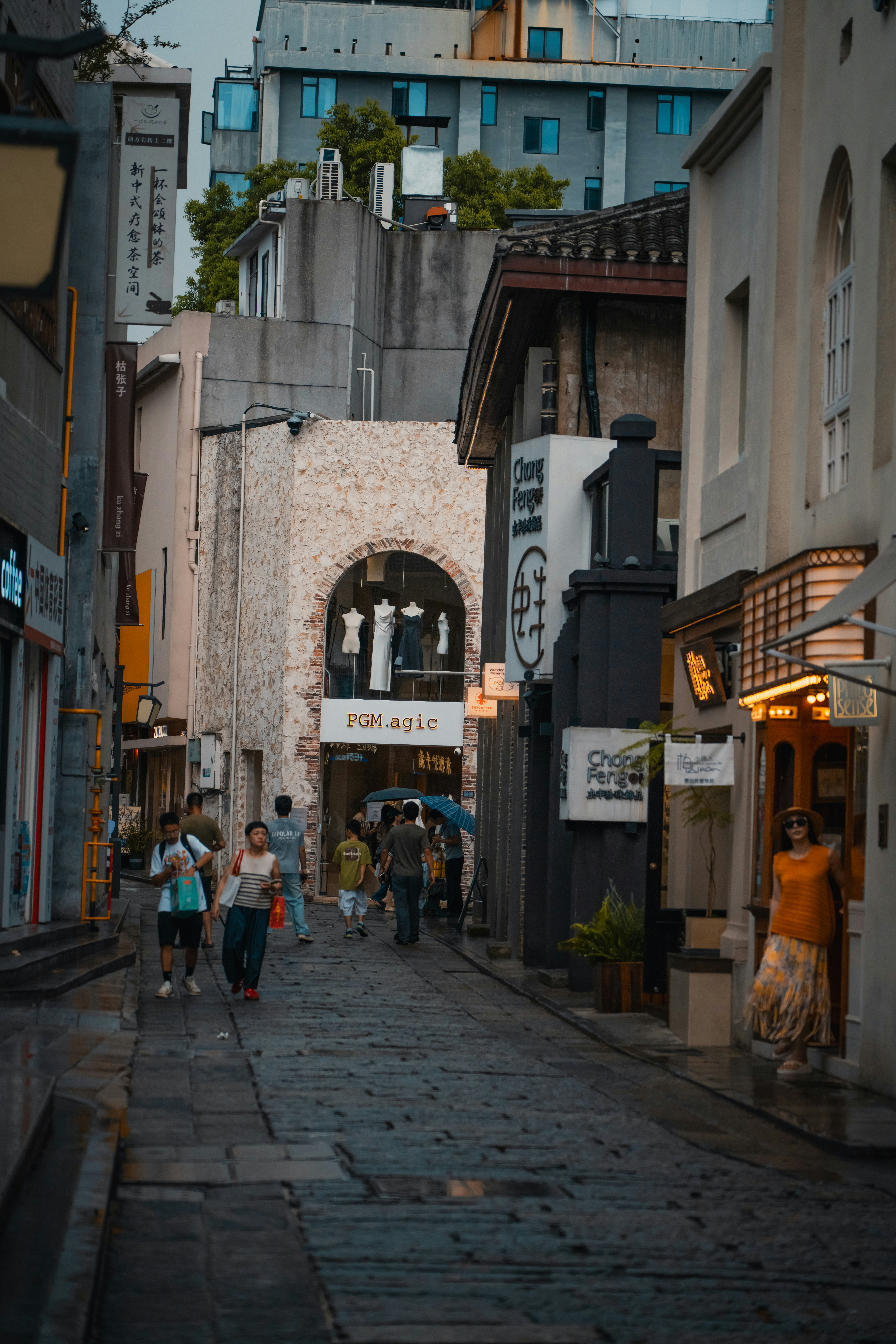 People walking along a narrow stone street lined with shops and storefronts