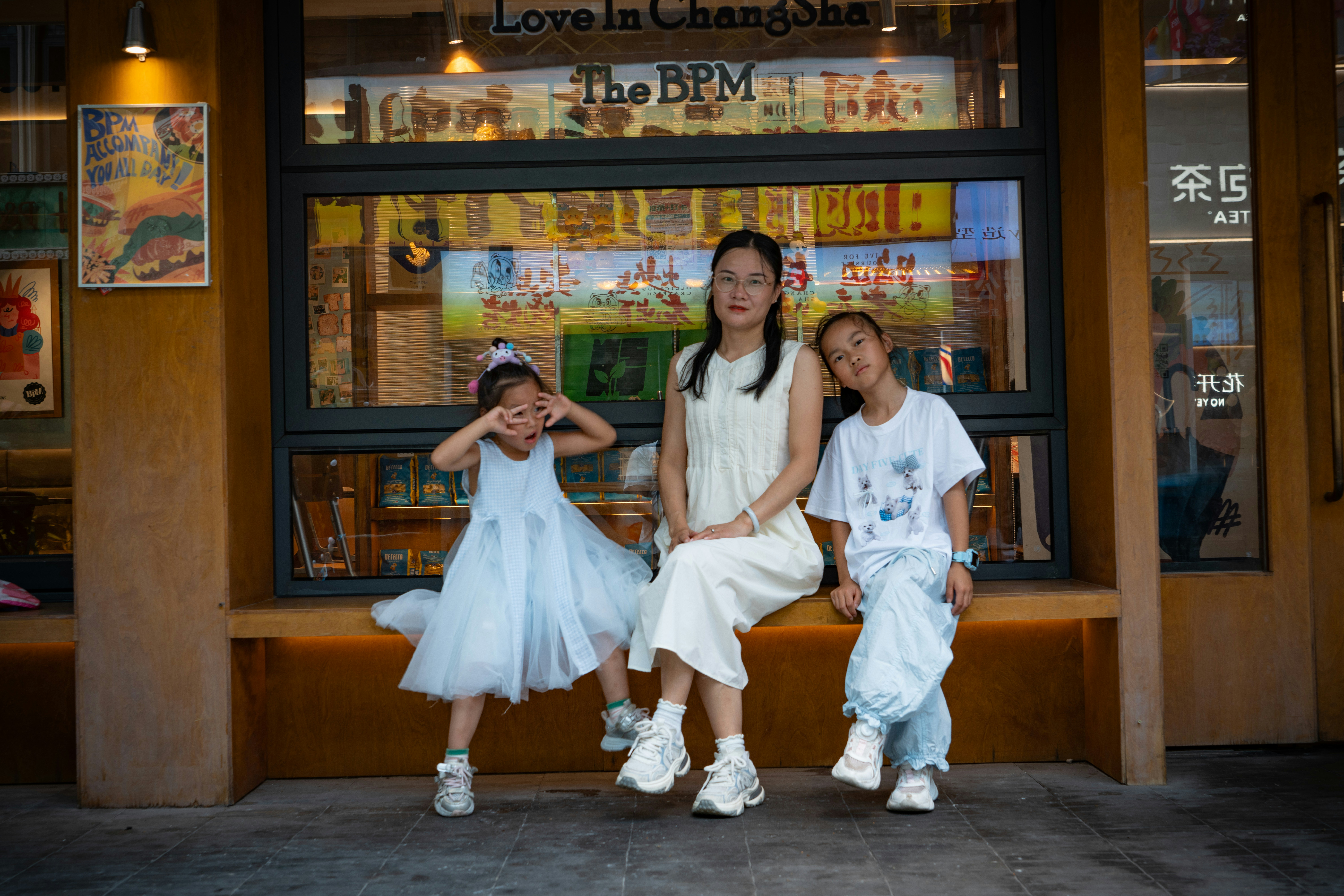A woman and two children sitting on a wooden bench in front of a shop