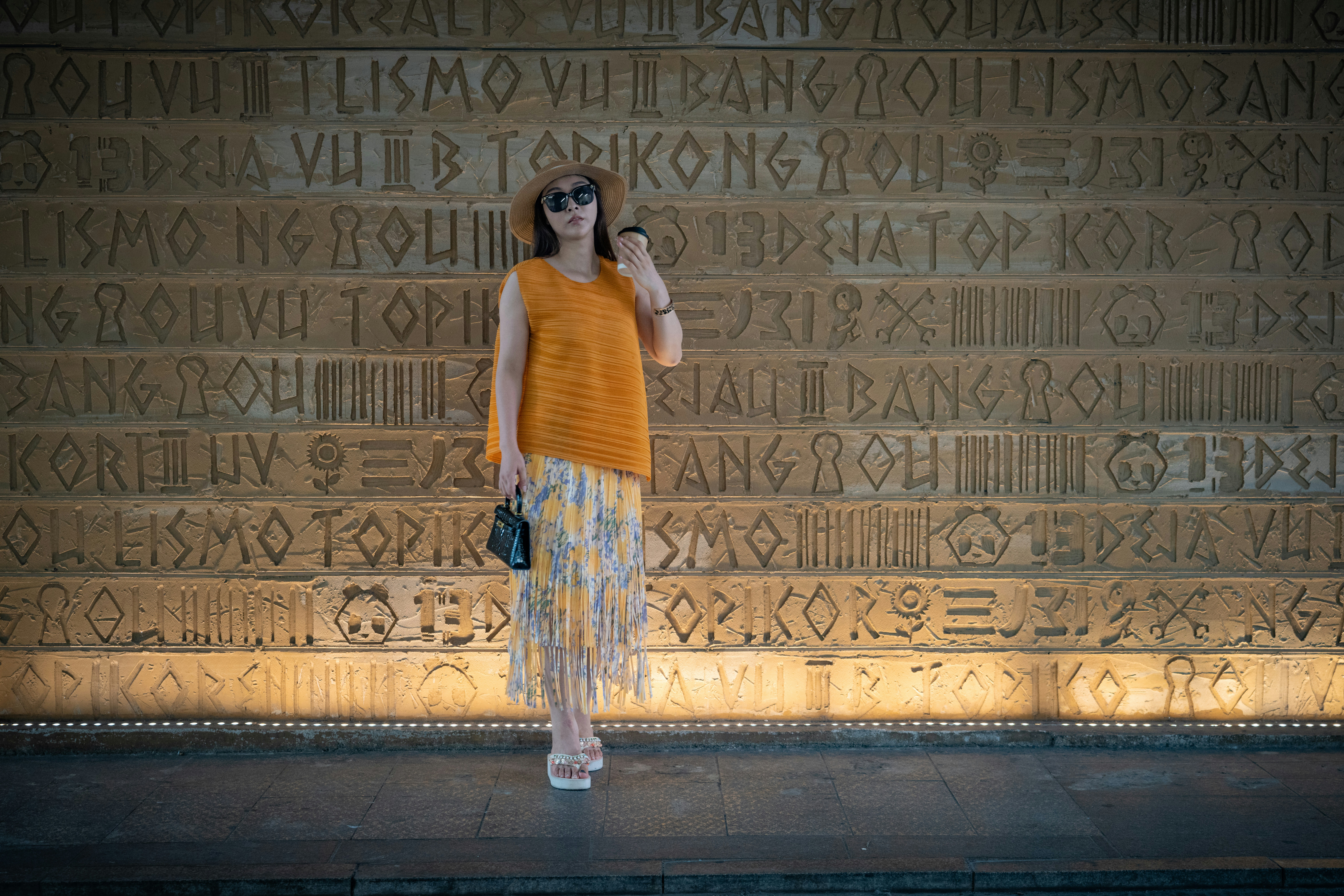 A woman in a straw hat and orange top standing before a carved wall