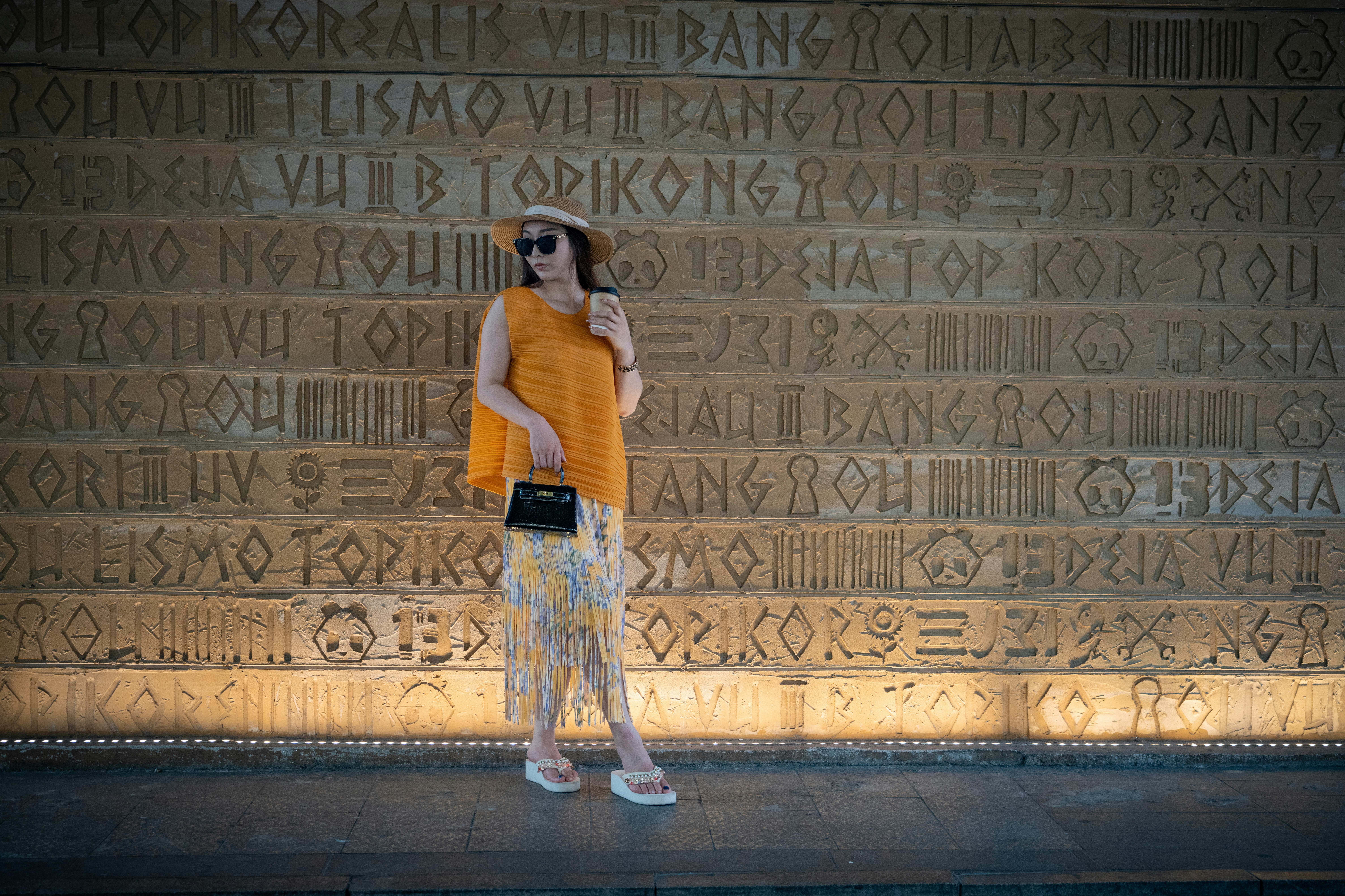 A woman in a straw hat and orange top standing before a carved wall