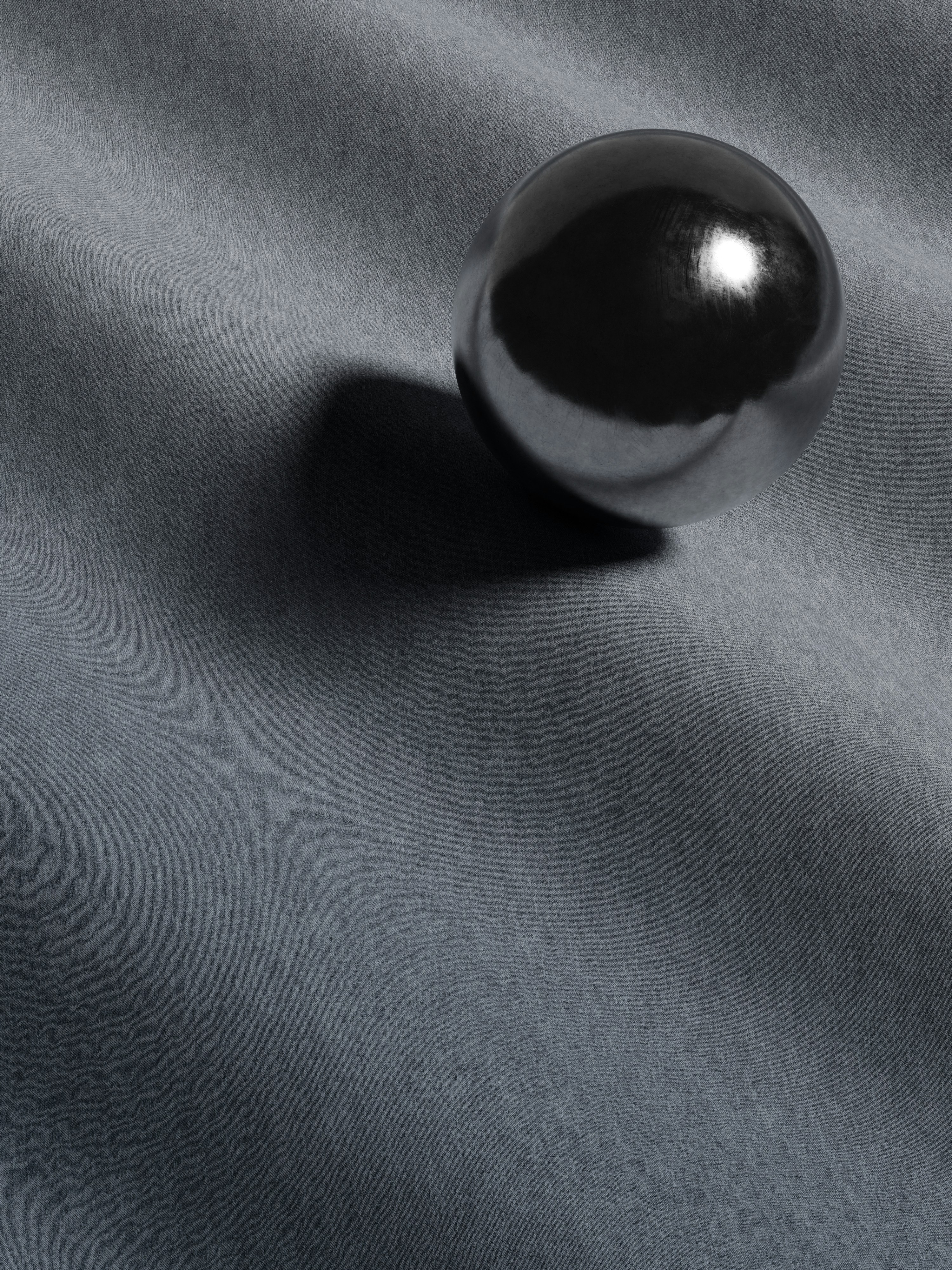 A polished dark sphere casting a sharp shadow on a grey fabric surface