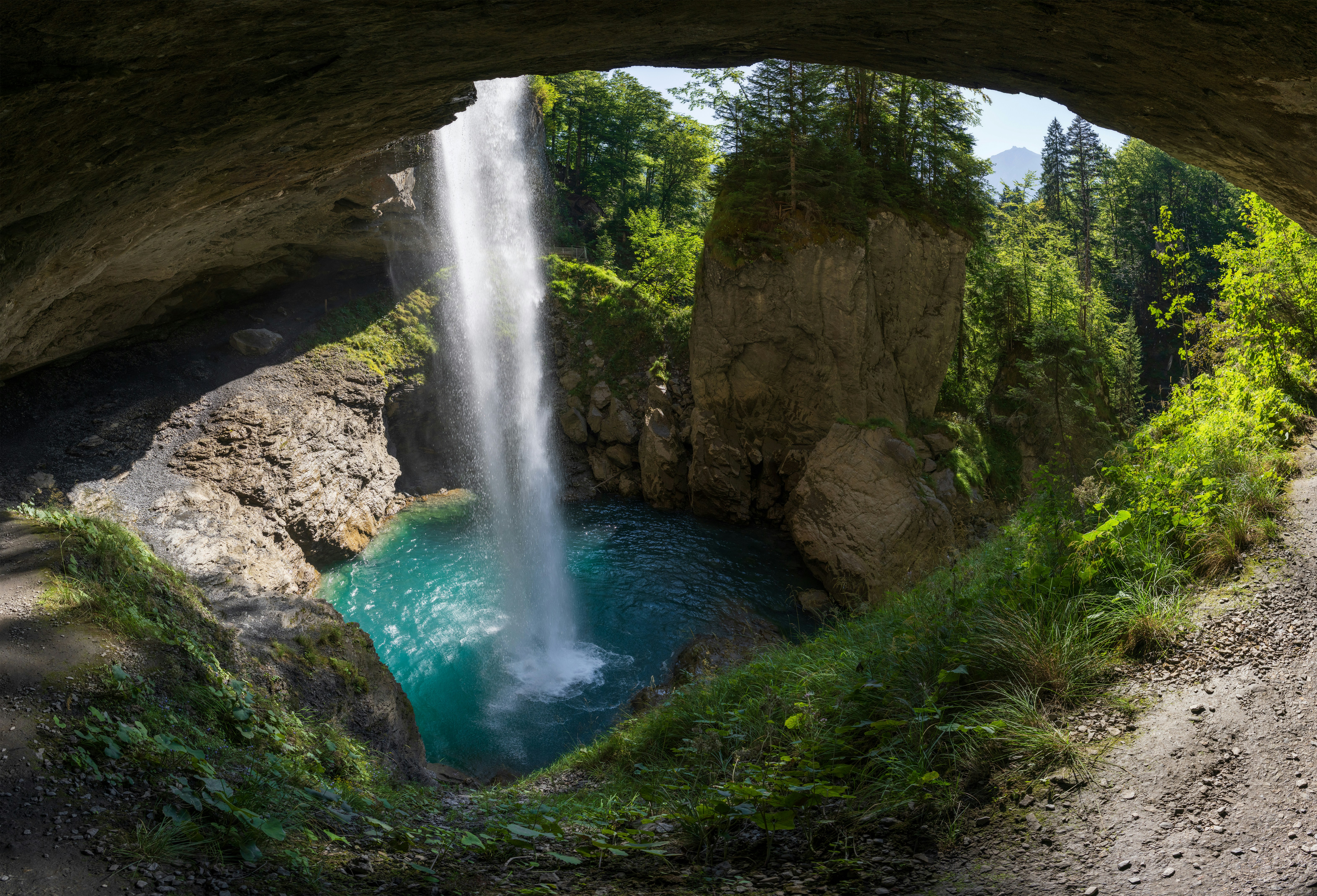 A waterfall cascading into a turquoise pool from a rocky cave opening