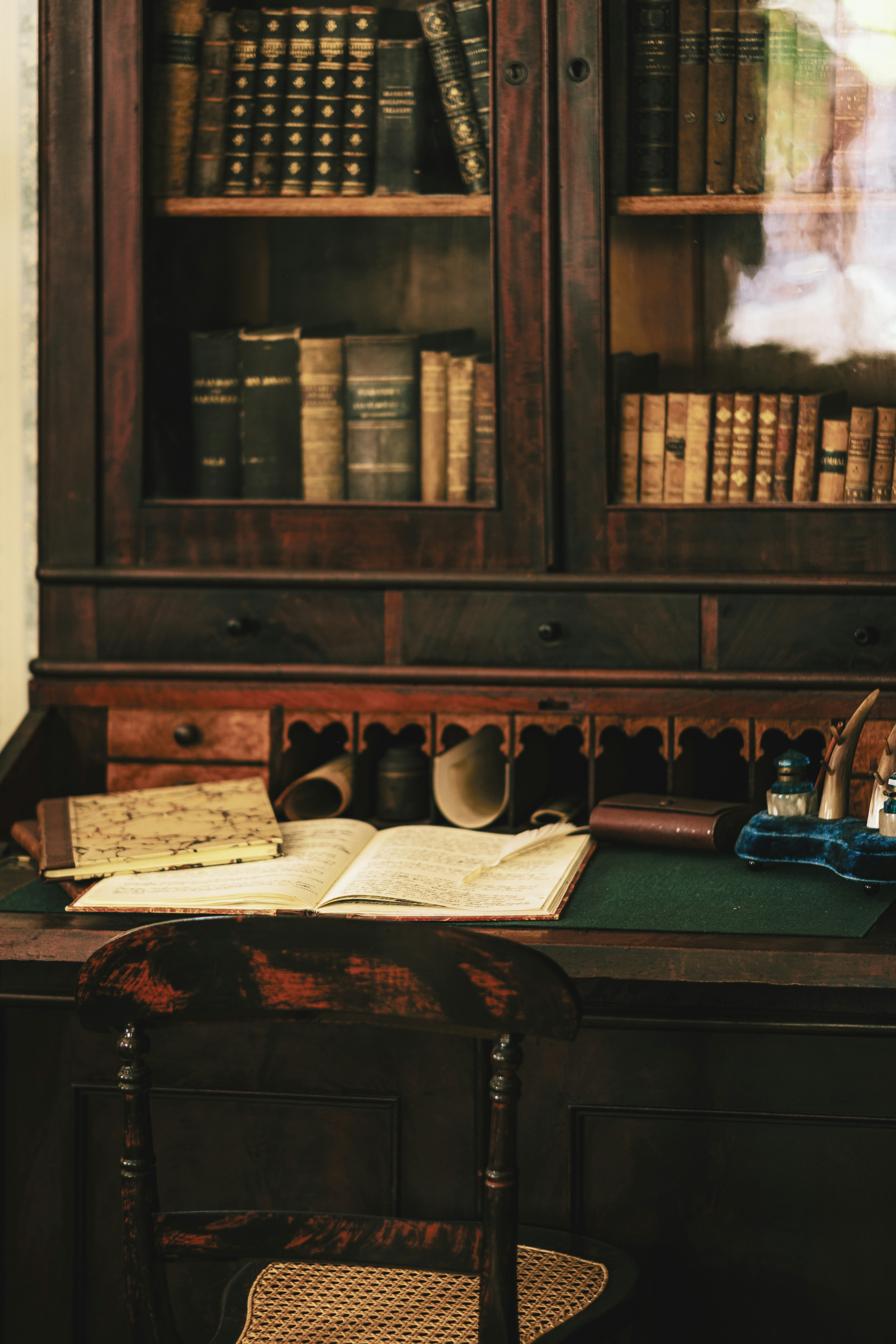 An open book with a quill on a wooden desk before a library cabinet