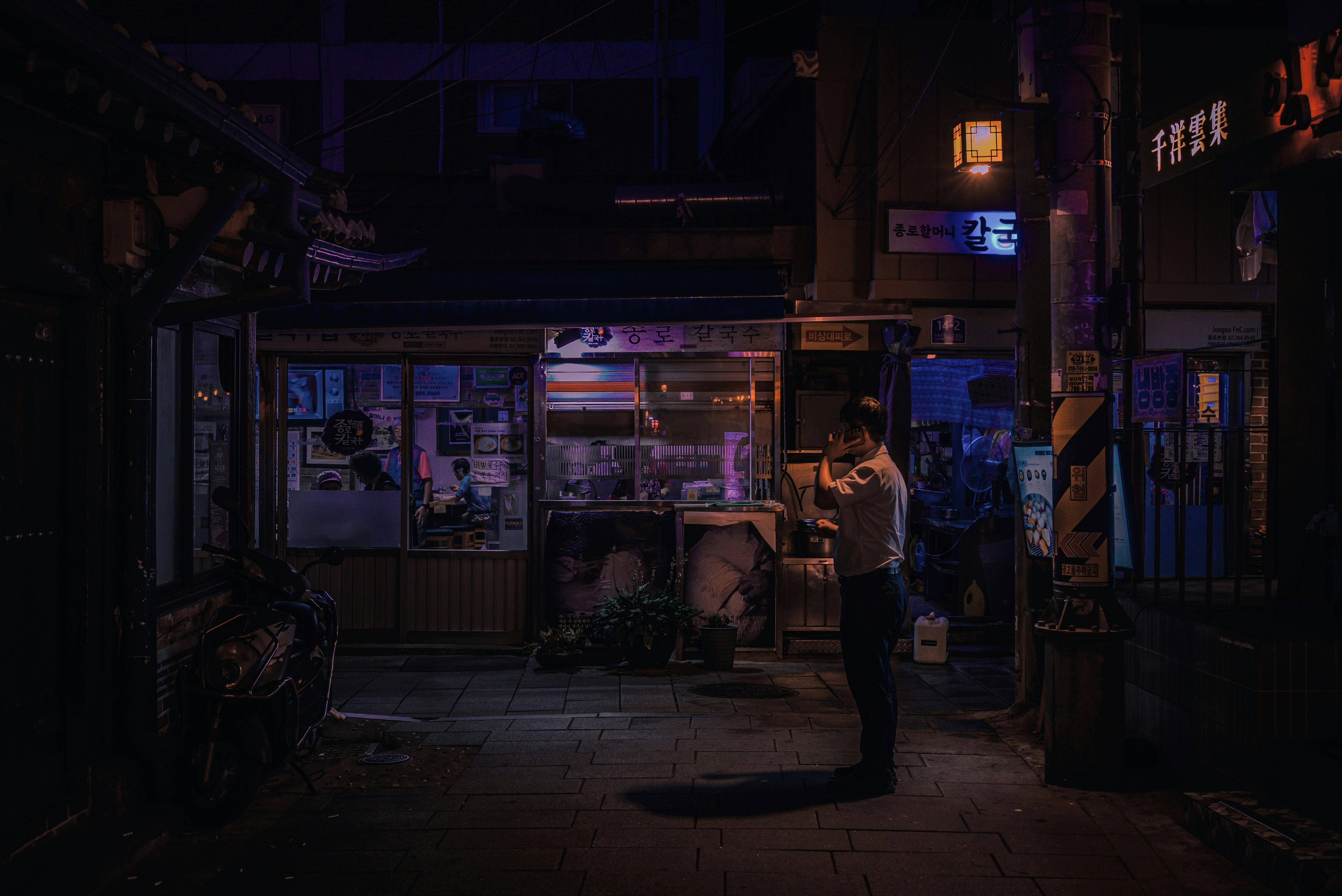 A person talking on a phone in a neon-lit alleyway at night