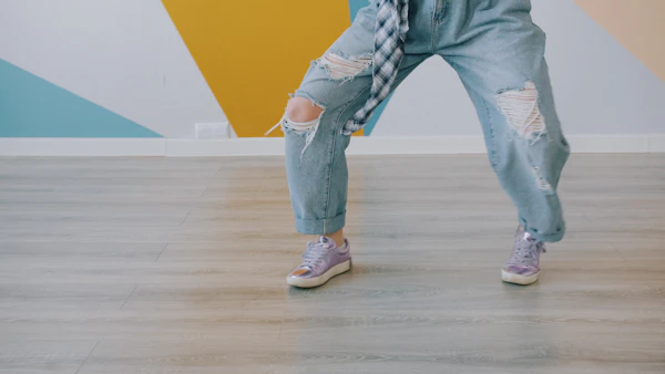 Les jambes d'une personne en jean et baskets sur un parquet de danse