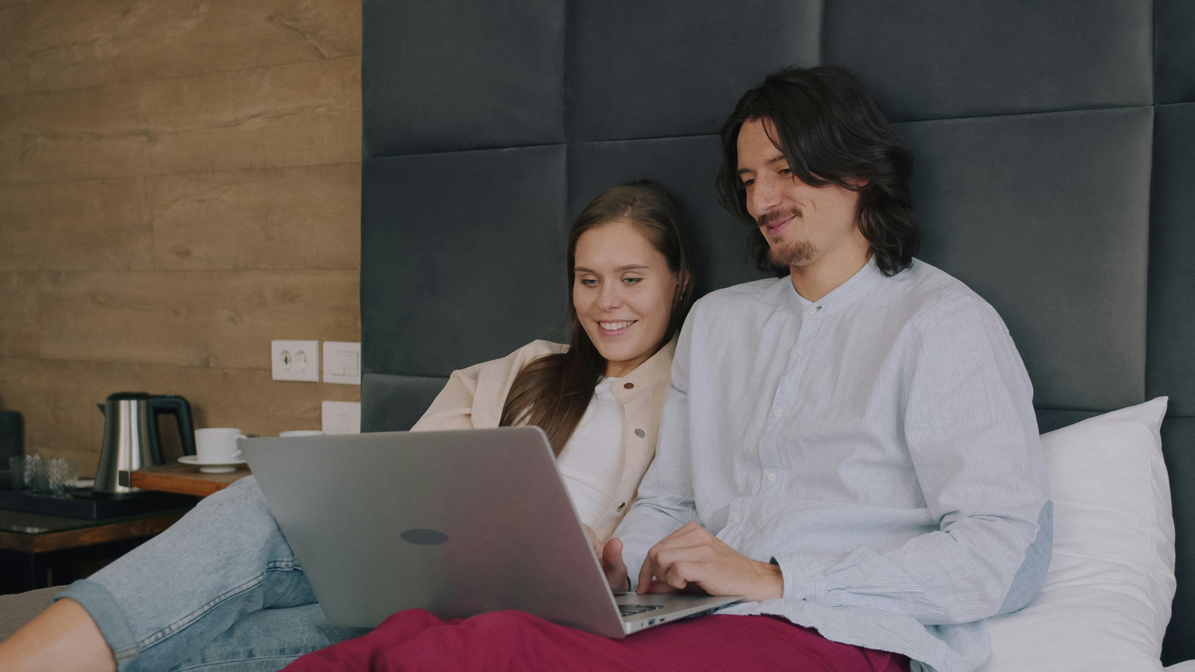 A man and a woman using a laptop while sitting on a bed