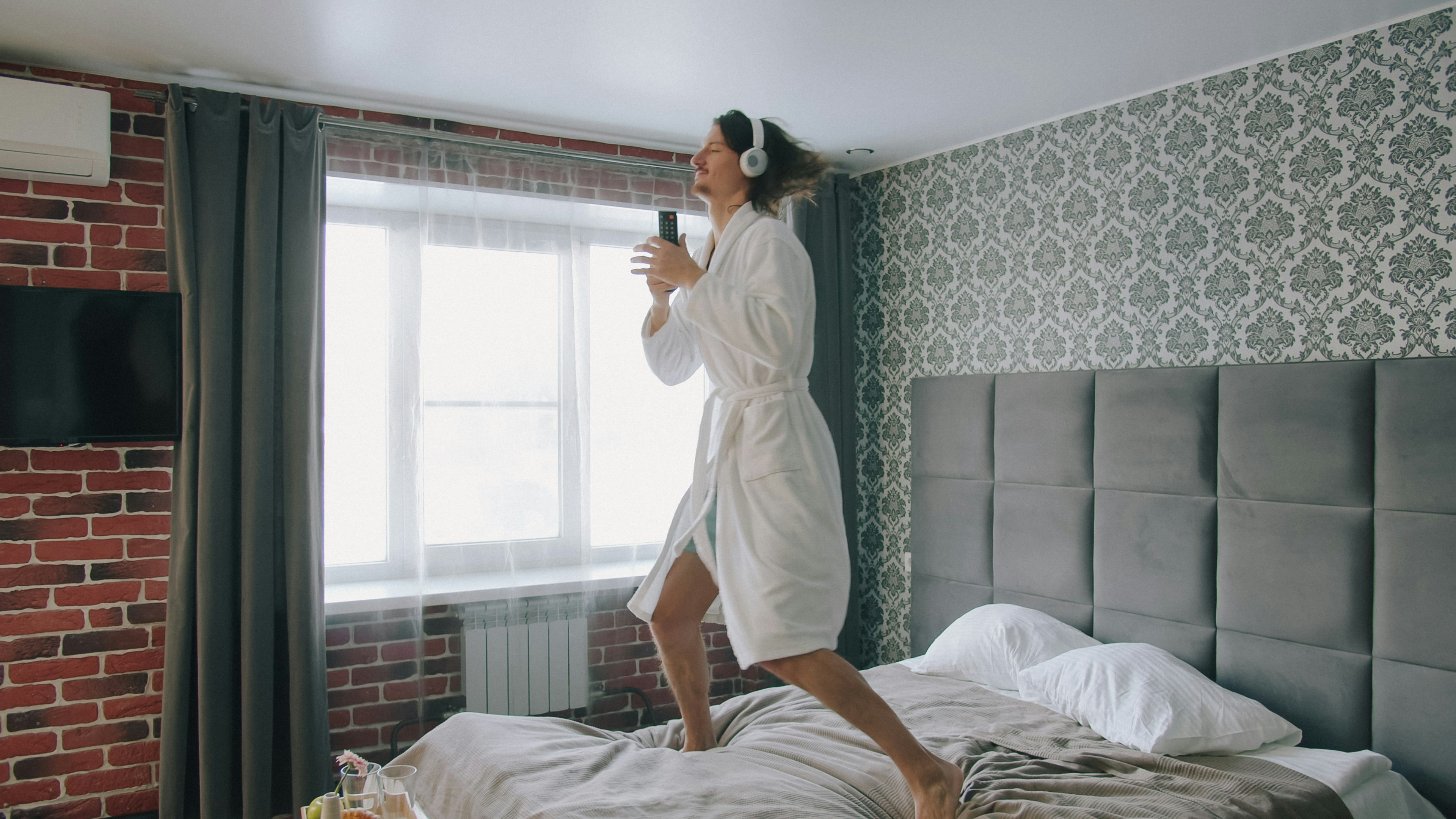 A person in a white bathrobe and headphones jumping on a bed