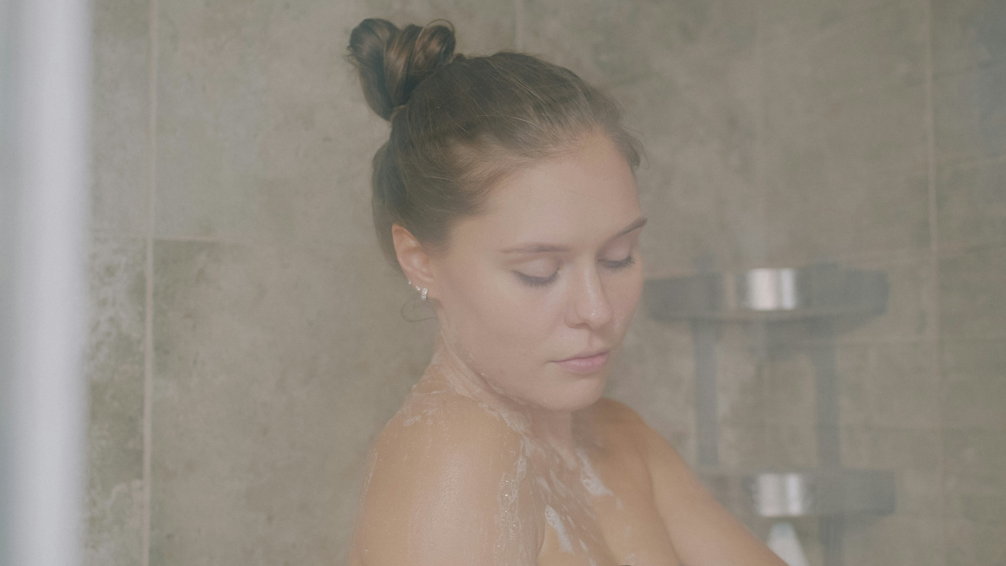 Beautiful young blond woman is washing in shower rubbing naked body with soap foam enjoying hygiene. Lifestyle, people and youth at home concept.
