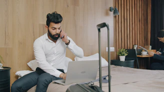 A man in a white shirt using a laptop while talking on a phone