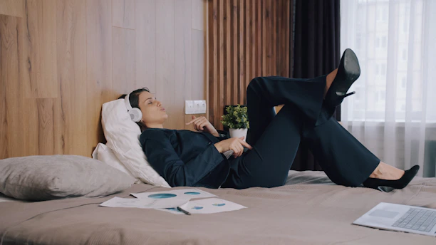 Woman lying on a bed in work clothes, listening to sound through headphones