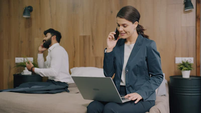 A woman in a blazer using a laptop while talking on a phone