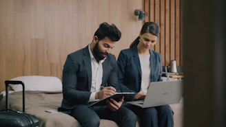 A man and a woman in business suits working on a hotel bed