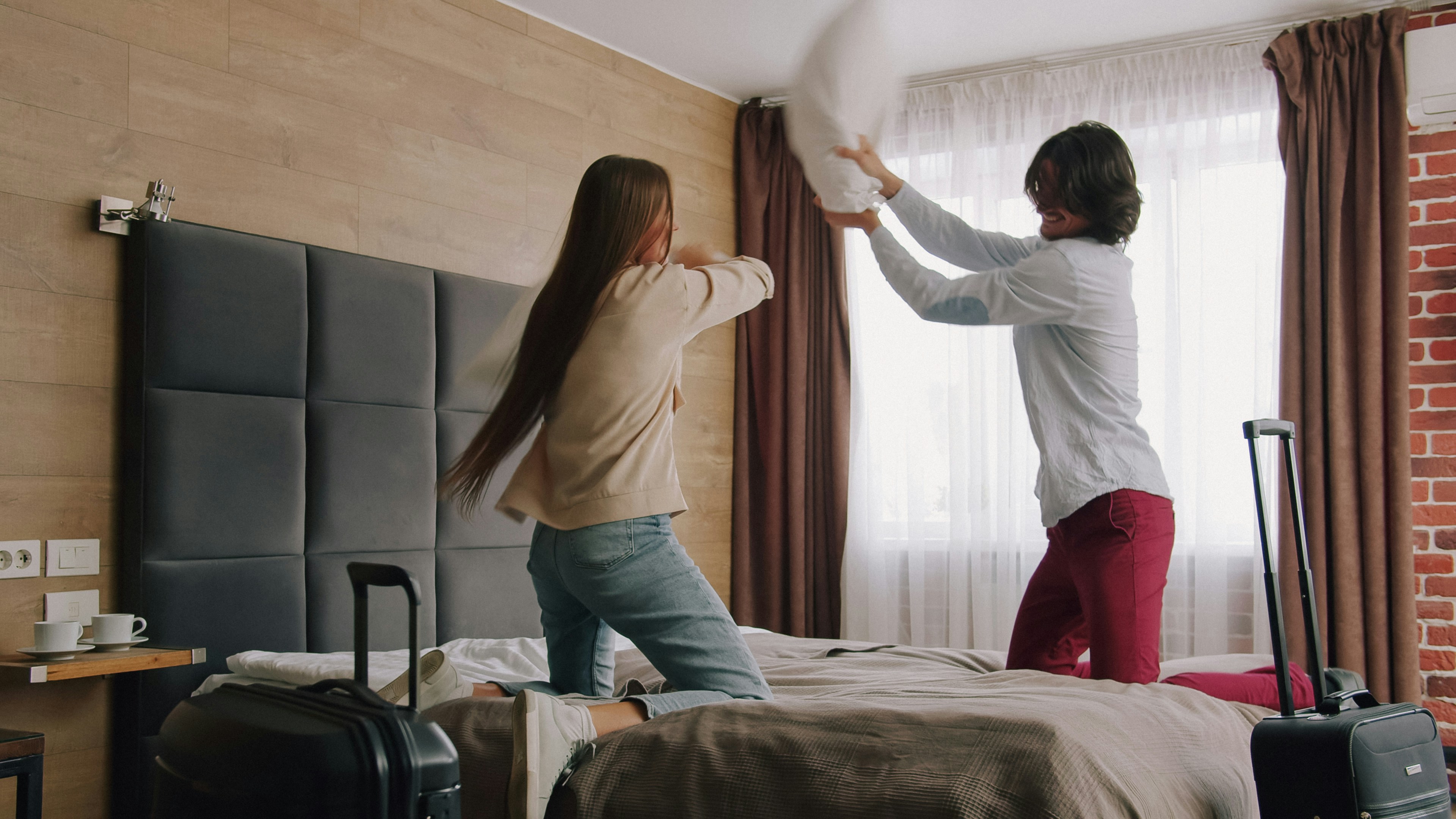 A woman and a man having a pillow fight on a hotel bed