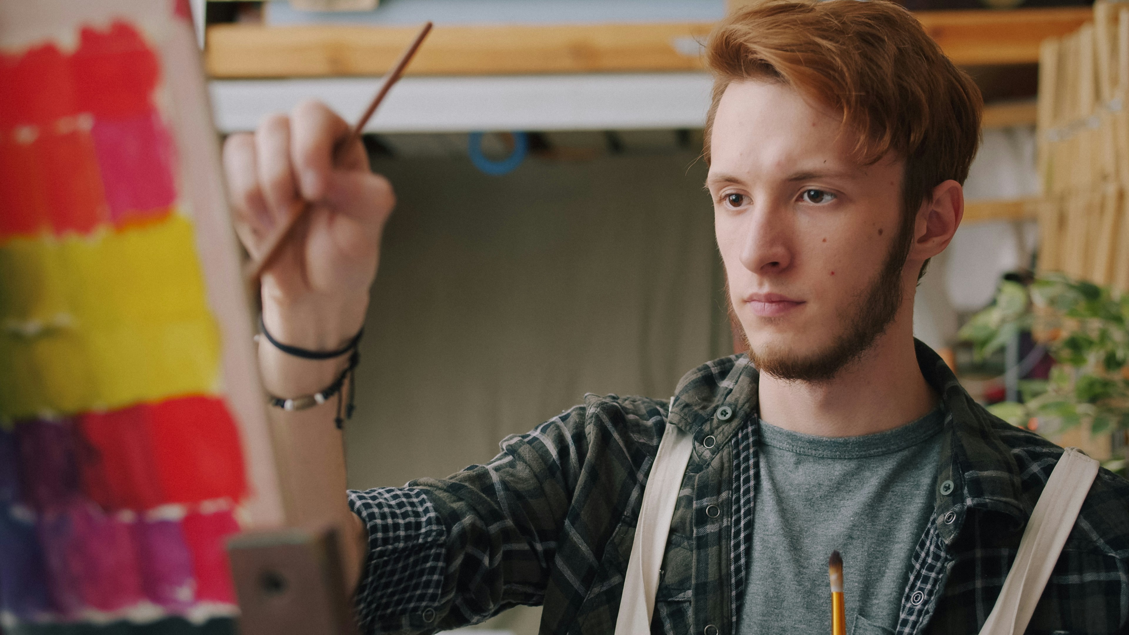 A man with red hair painting colorful squares on a canvas in a studio