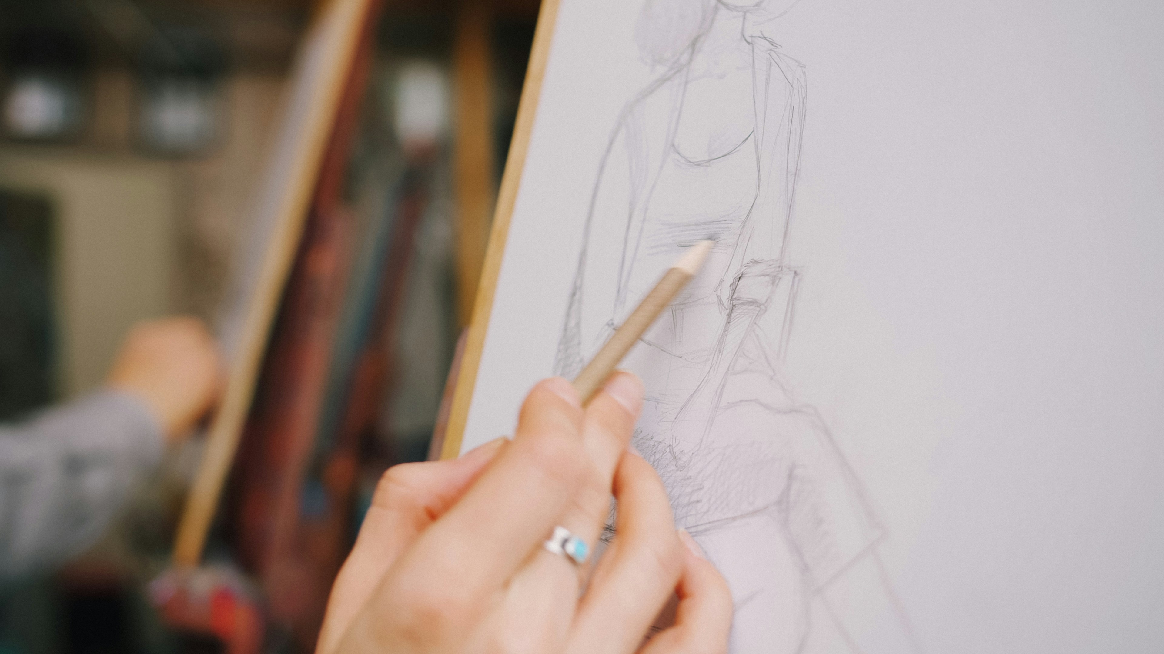 A hand holding a pencil sketching a figure on a white paper