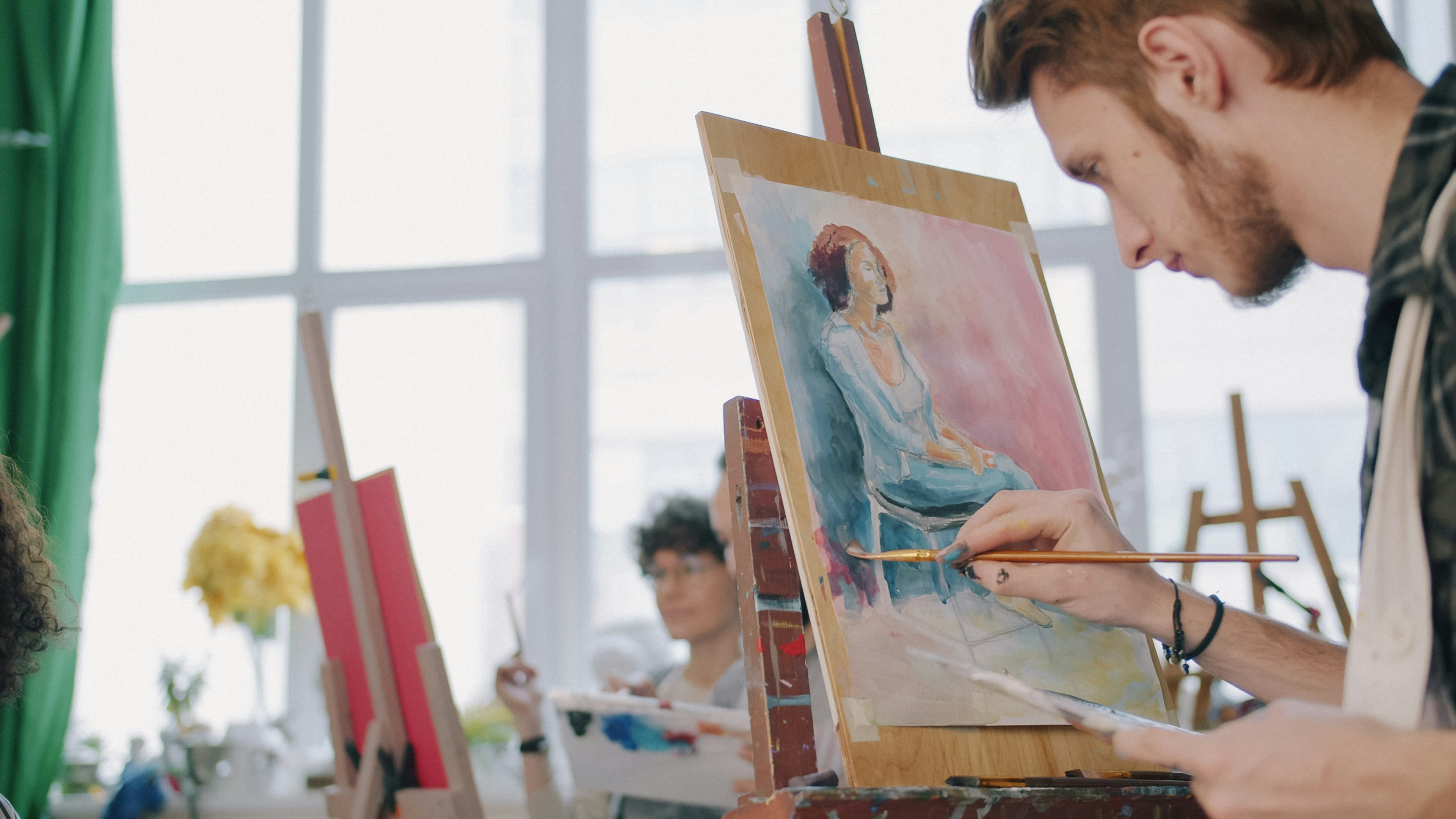 A person painting a portrait on a canvas in a bright art studio
