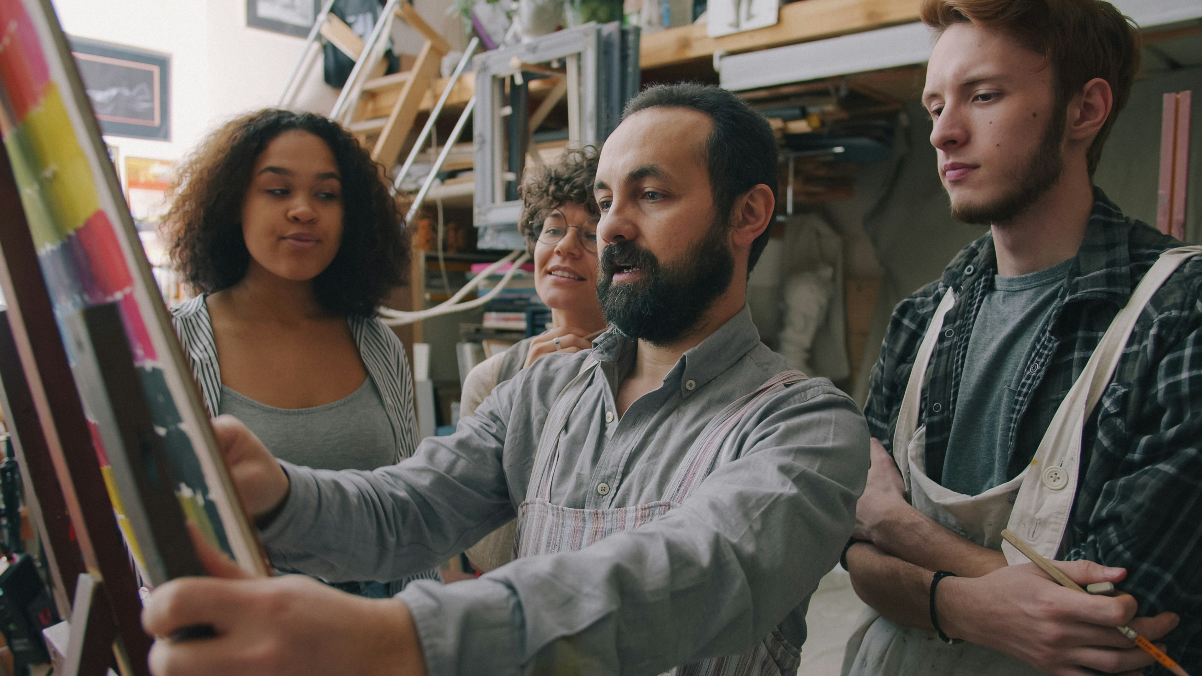 A man in an apron teaching three students in an art studio